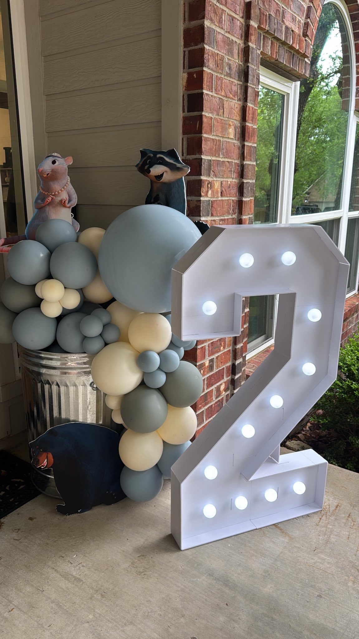 Light-up marquee number two beside a festive balloon arch and woodland creature decorations for a second birthday.