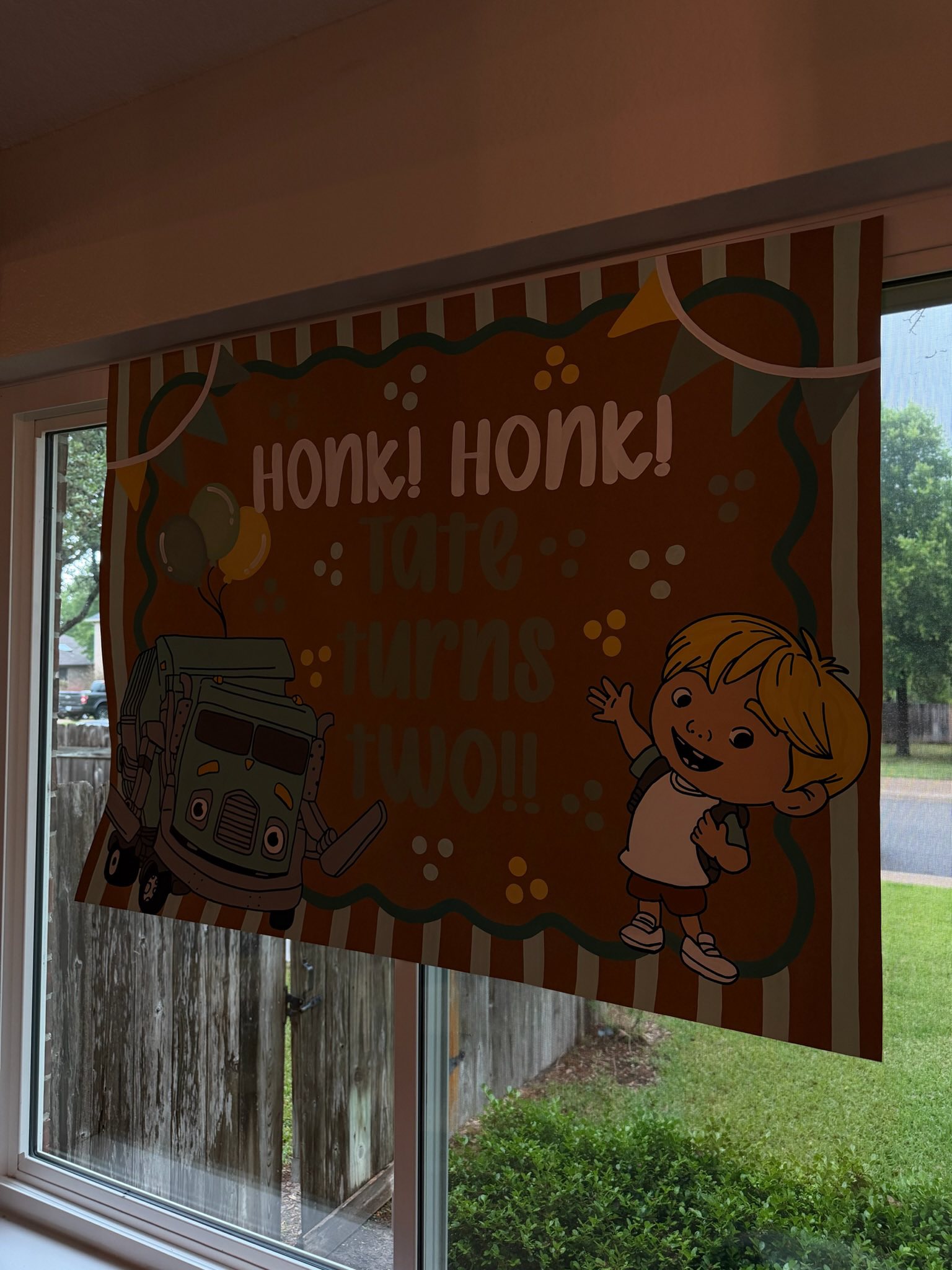 Tate turns two birthday window sign featuring a garbage truck and illustration of a boy waving