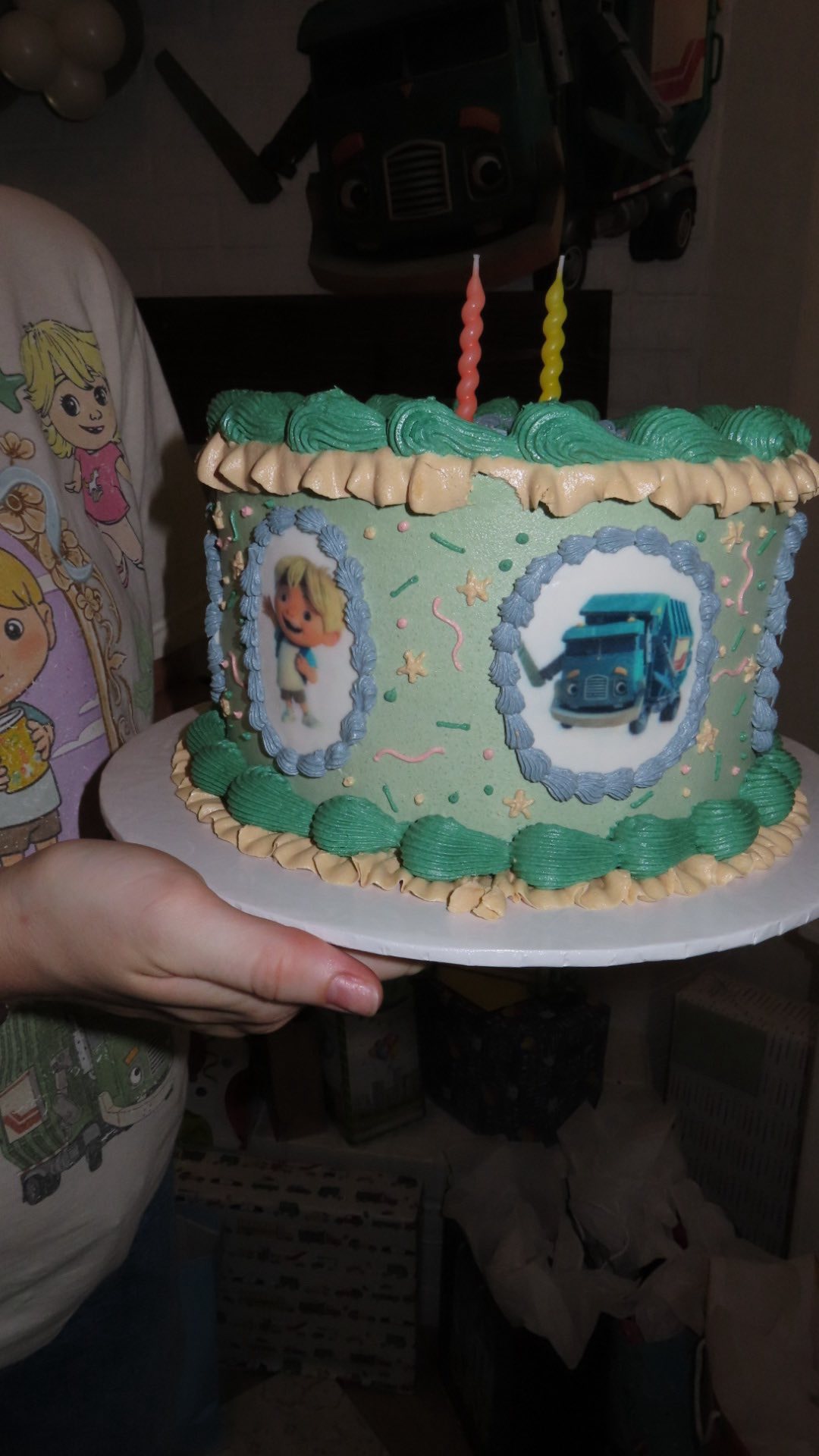 Birthday cake decorated with green frosting, star sprinkles, and edible imagery of a boy and a garbage truck.