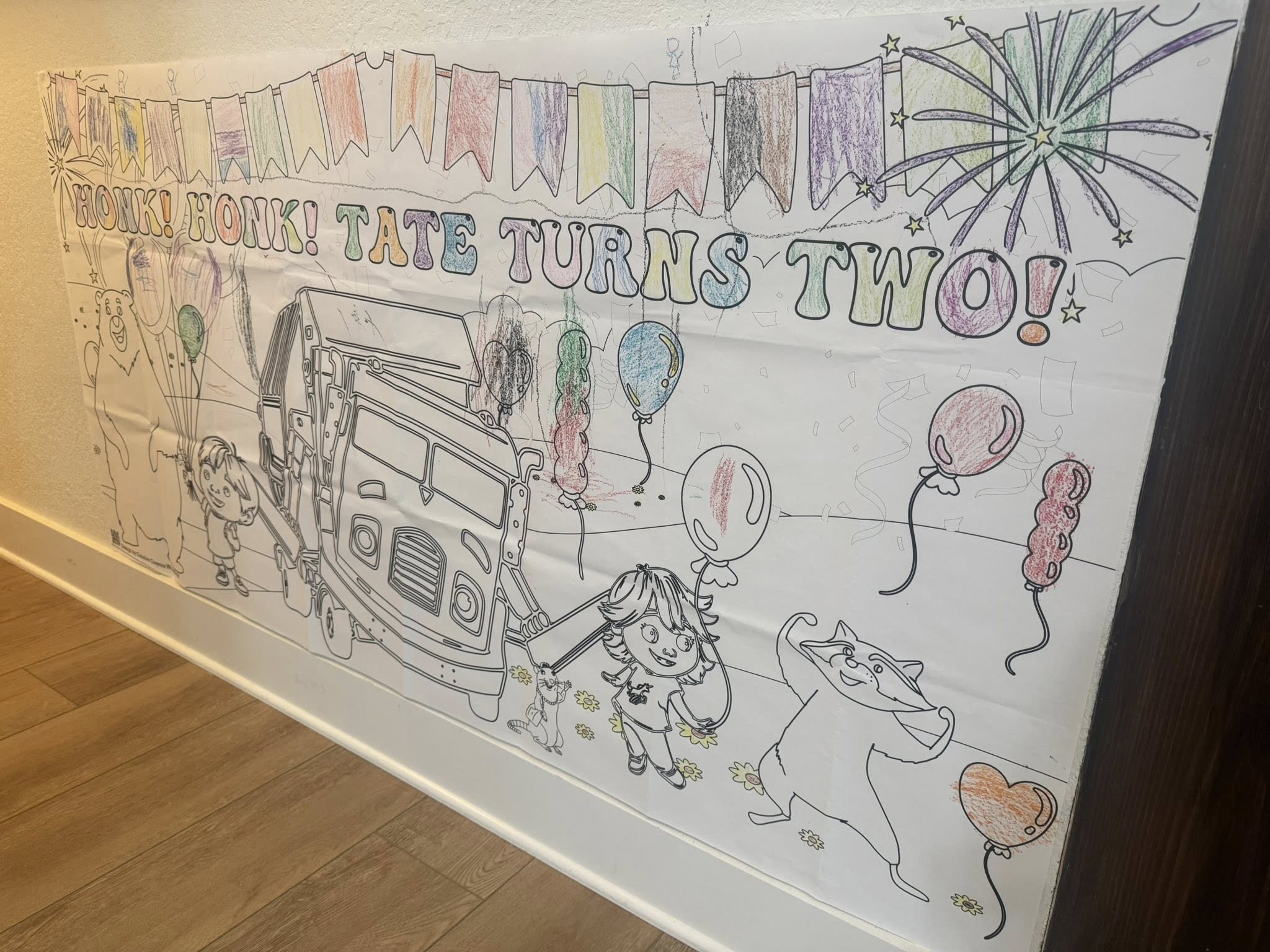 Giant coloring poster with banner reading Tate Turns Two featuring a garbage truck, balloons, and cartoon animals