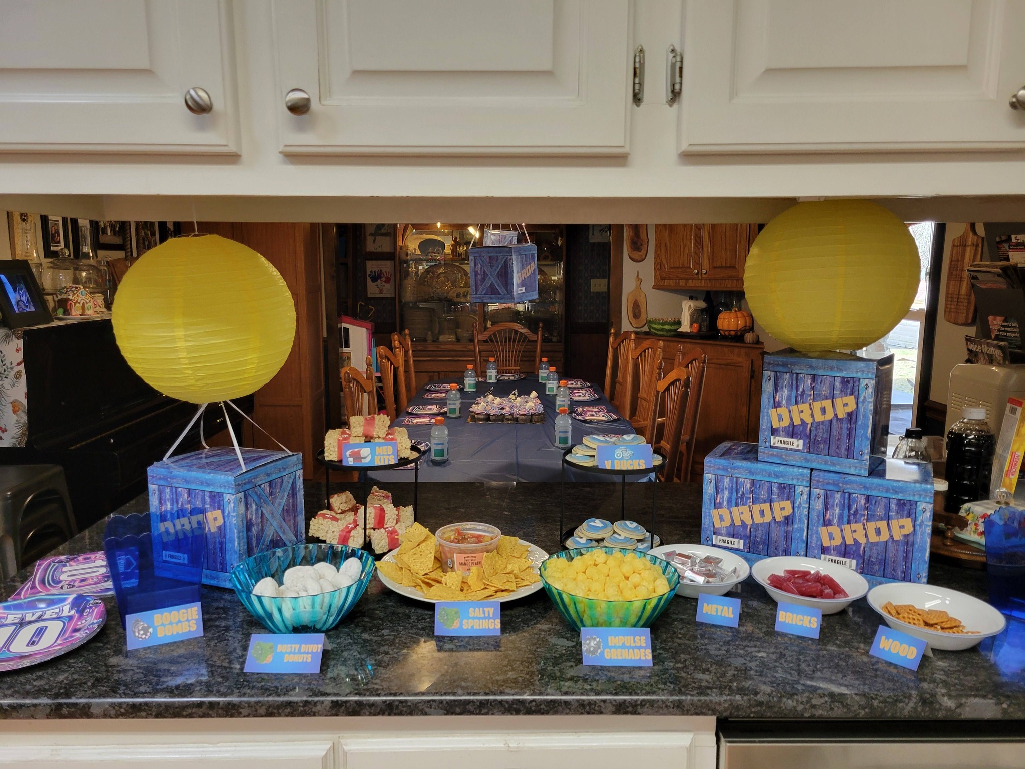 Fortnite-themed party snack table with labeled treats like Med Kits, V-Bucks, and supply drop boxes.
