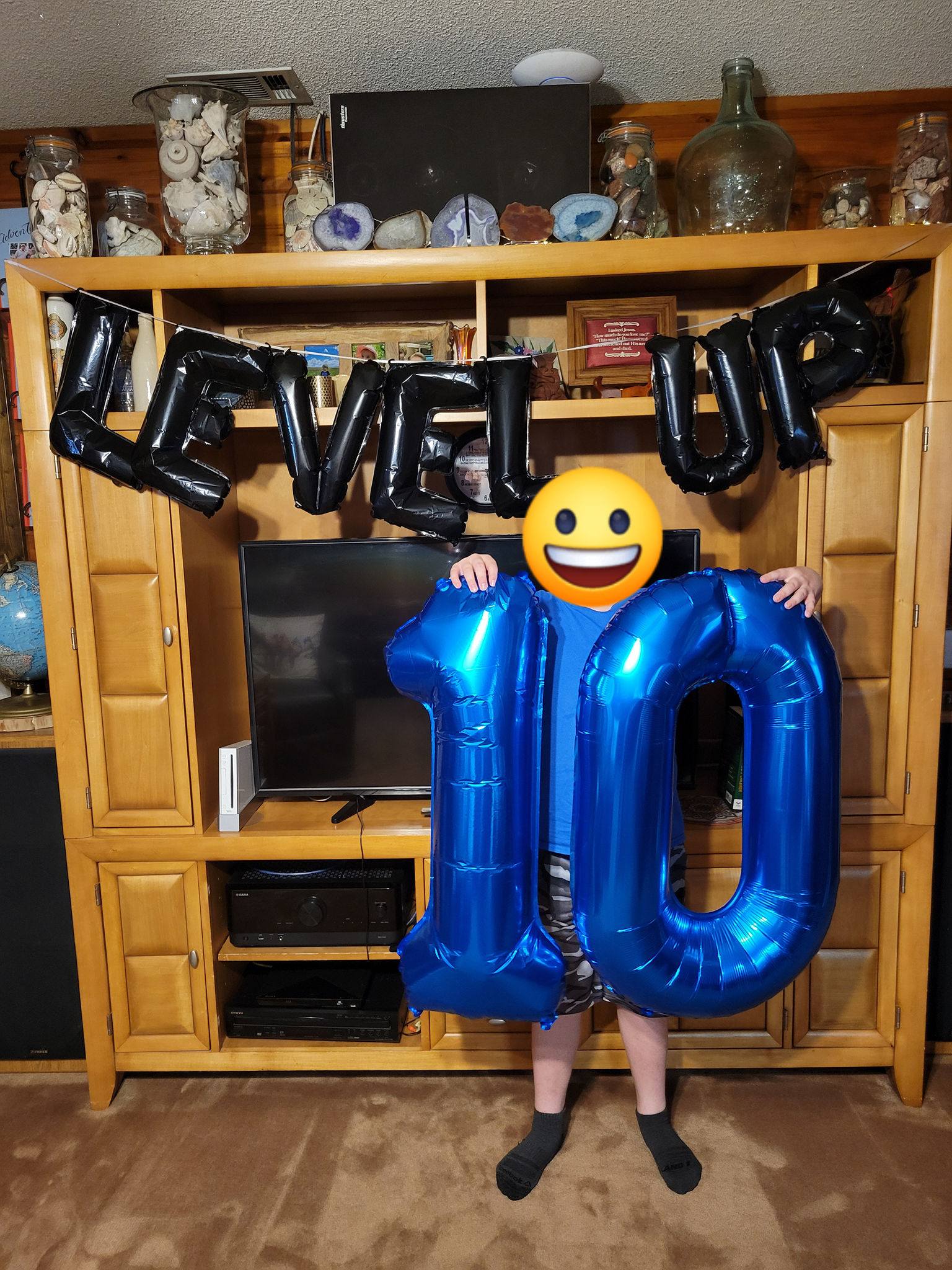 Child holding large blue number 10 balloons in front of a Level Up banner for a 10th birthday celebration.