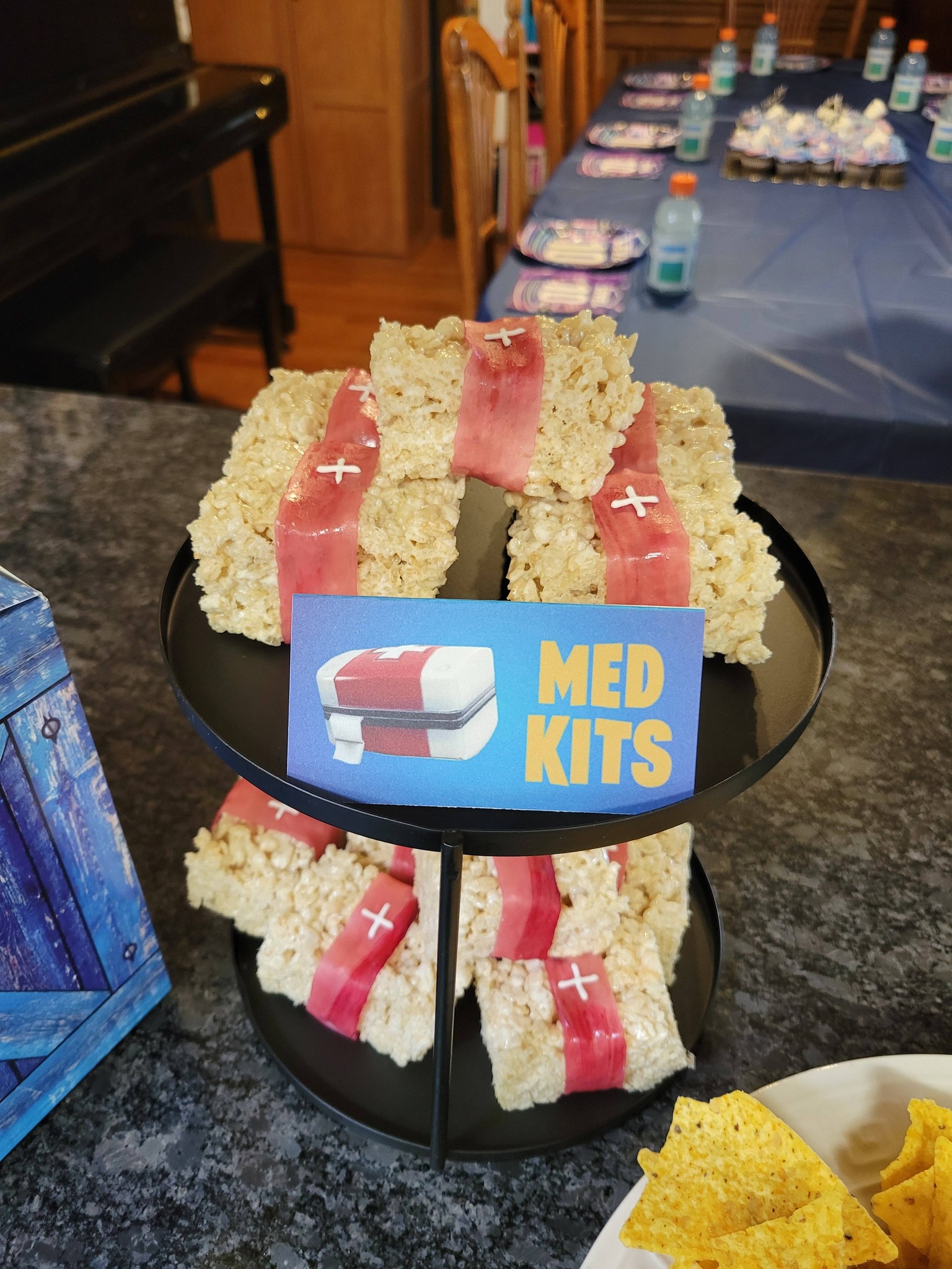 Rice Krispie treats decorated as med kits with red candy ribbons and white plus signs on a two-tier display stand.
