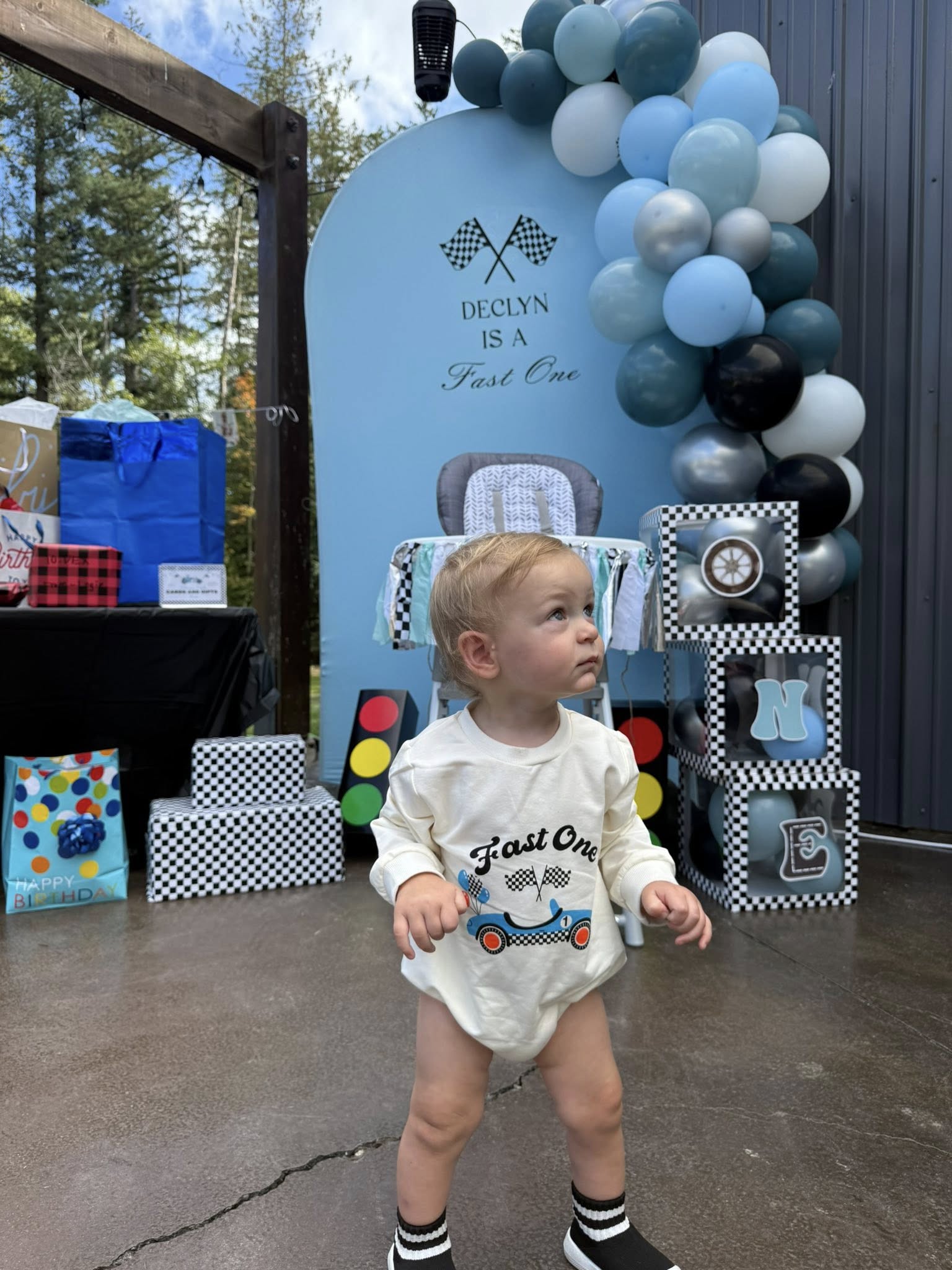 Toddler wearing a Fast One racing-themed outfit standing in front of a blue first birthday party backdrop.