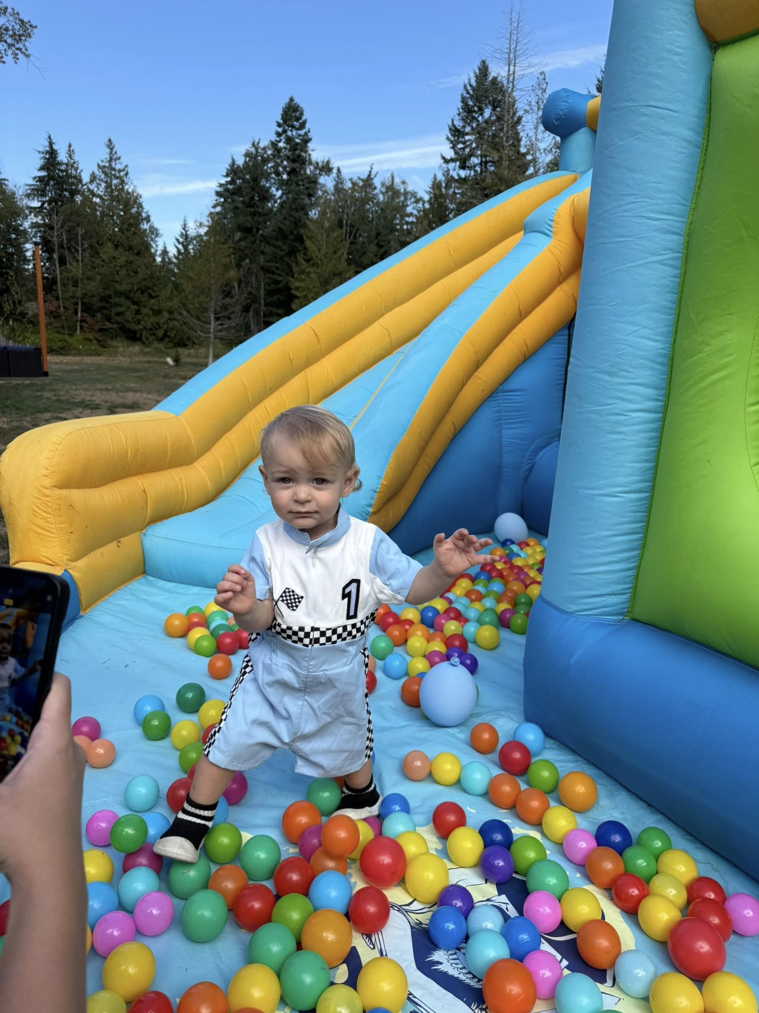 Toddler in race car themed outfit standing in a colorful ball pit inside an inflatable bouncer