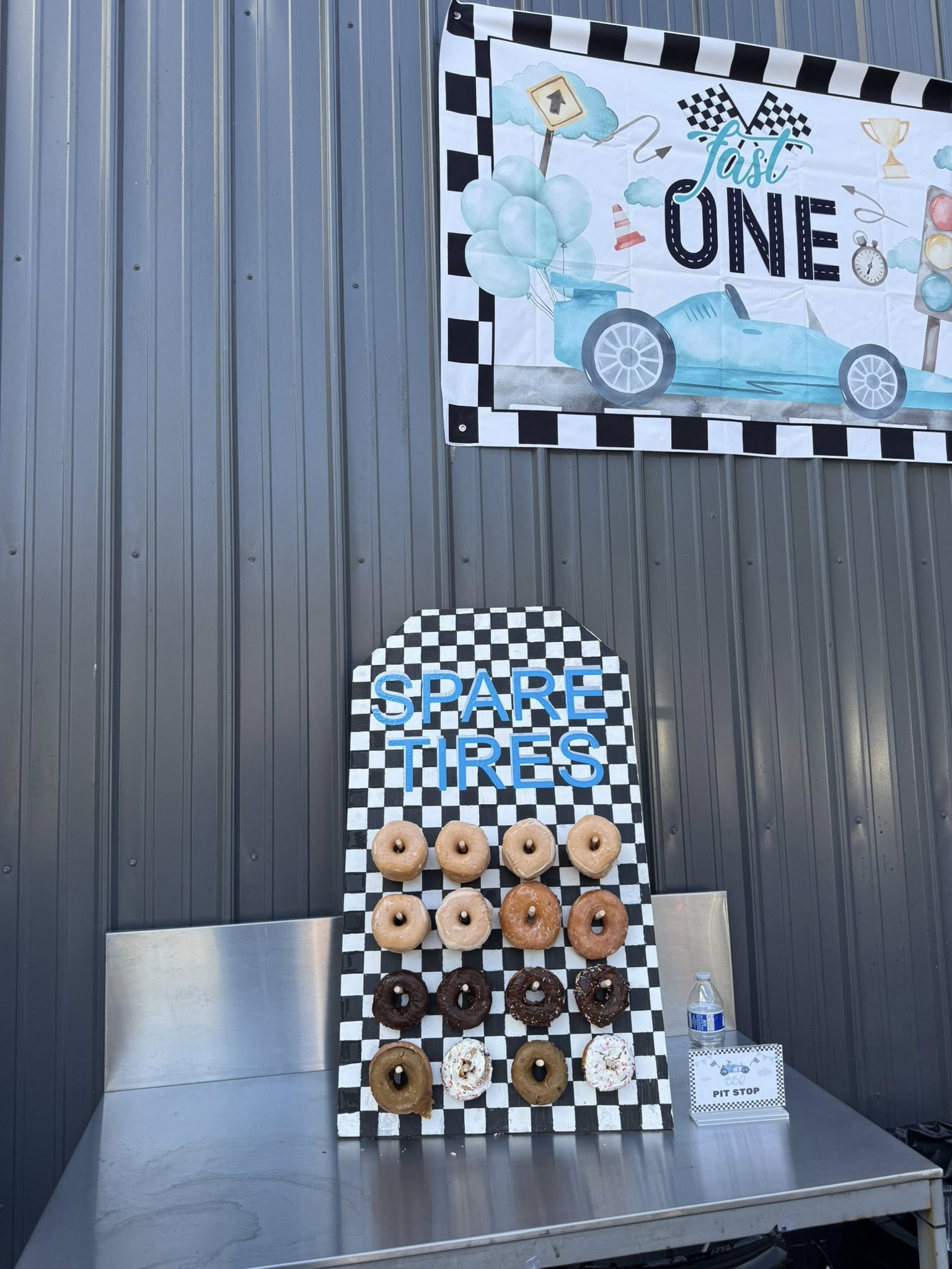 Race car-themed party donut wall displaying assorted glazed and chocolate donuts under a Fast One banner.