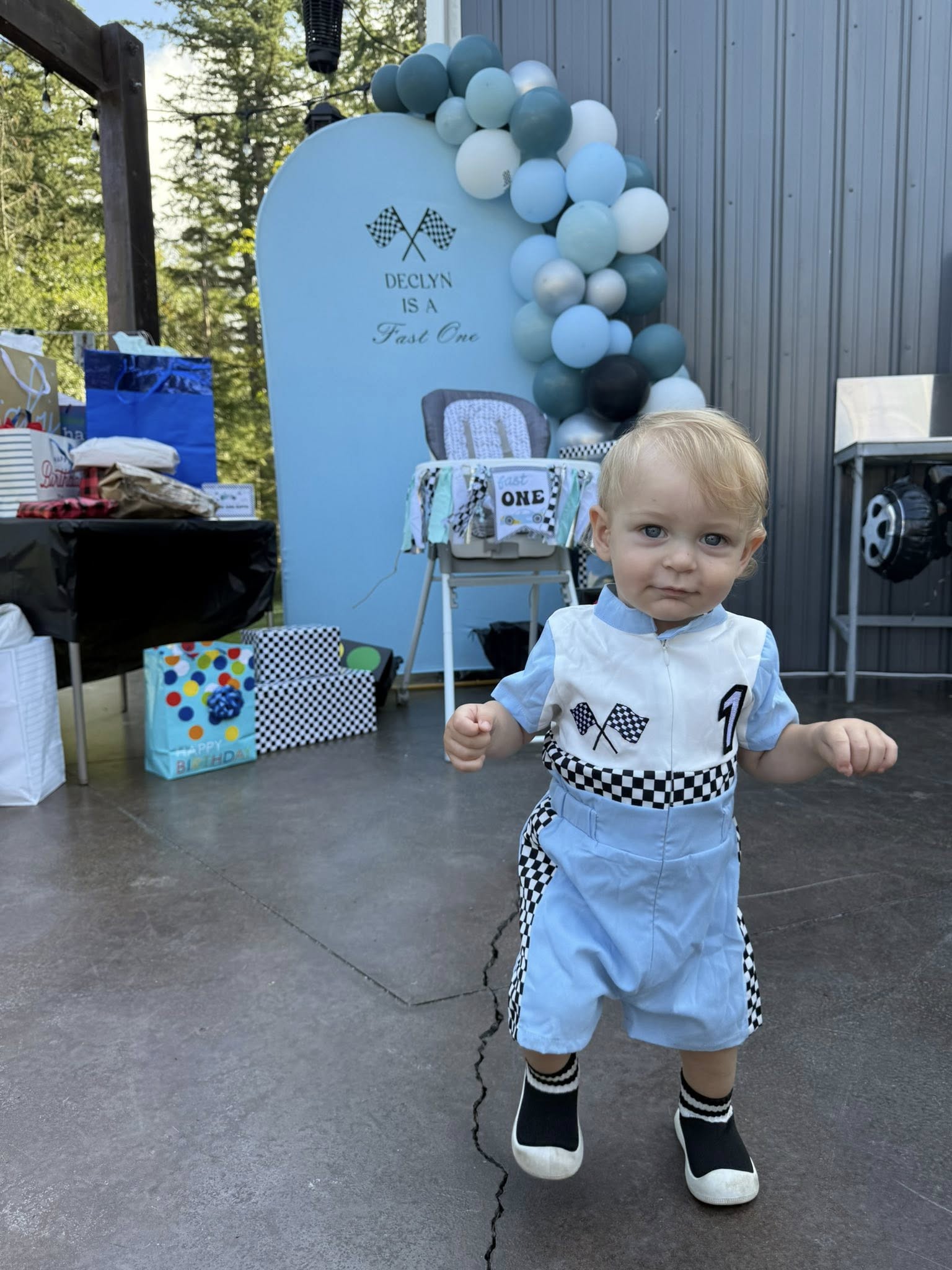 Toddler wearing a racing-themed outfit at a 'Fast One' first birthday party with blue decorations.