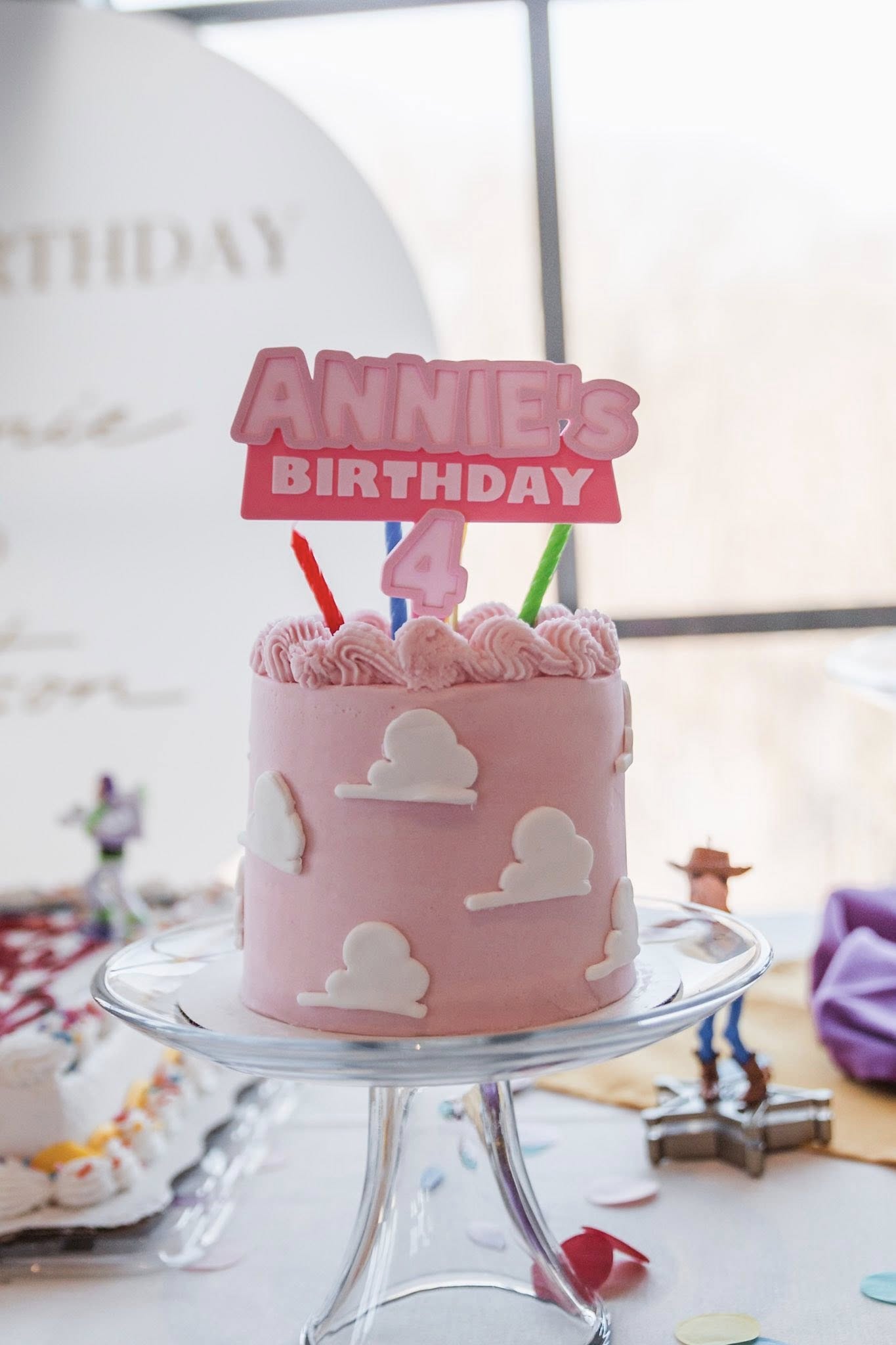 Pink birthday cake decorated with Toy Story-inspired clouds and a custom Annie's 4th birthday topper.