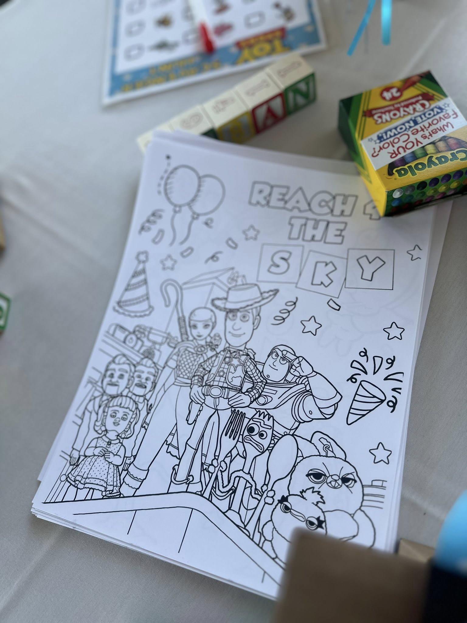 Toy Story coloring page featuring Woody, Buzz Lightyear, and other characters, next to a box of Crayola crayons