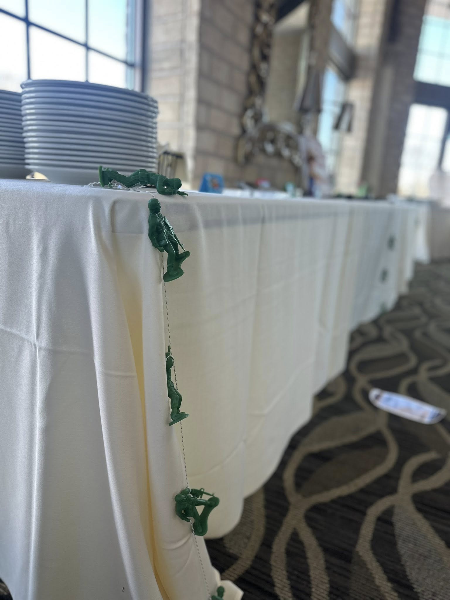 Green plastic army men toy string decoration hanging from a table covered in a white tablecloth.