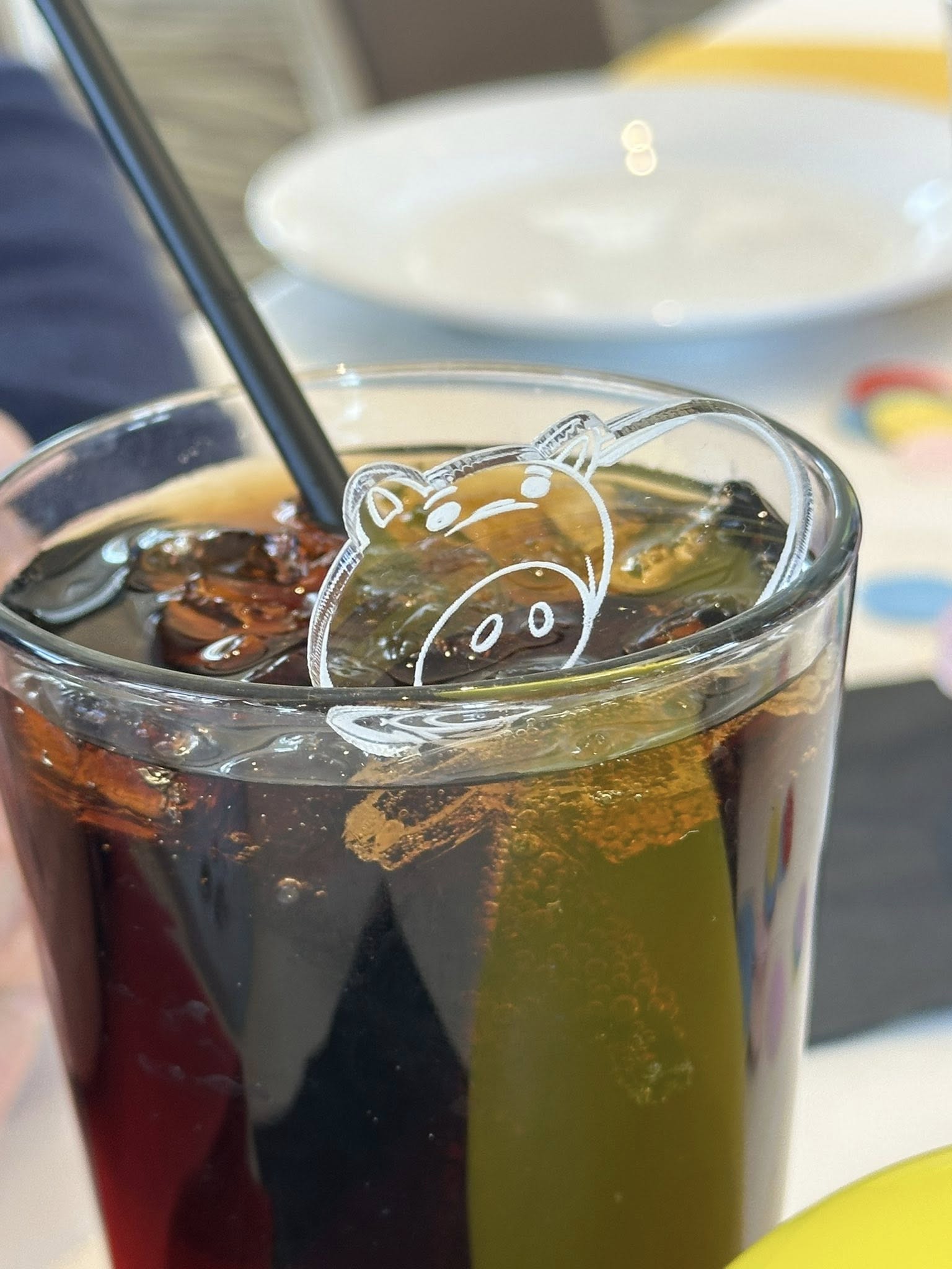 Glass of soda with an acrylic pig-shaped drink marker resting on the rim.