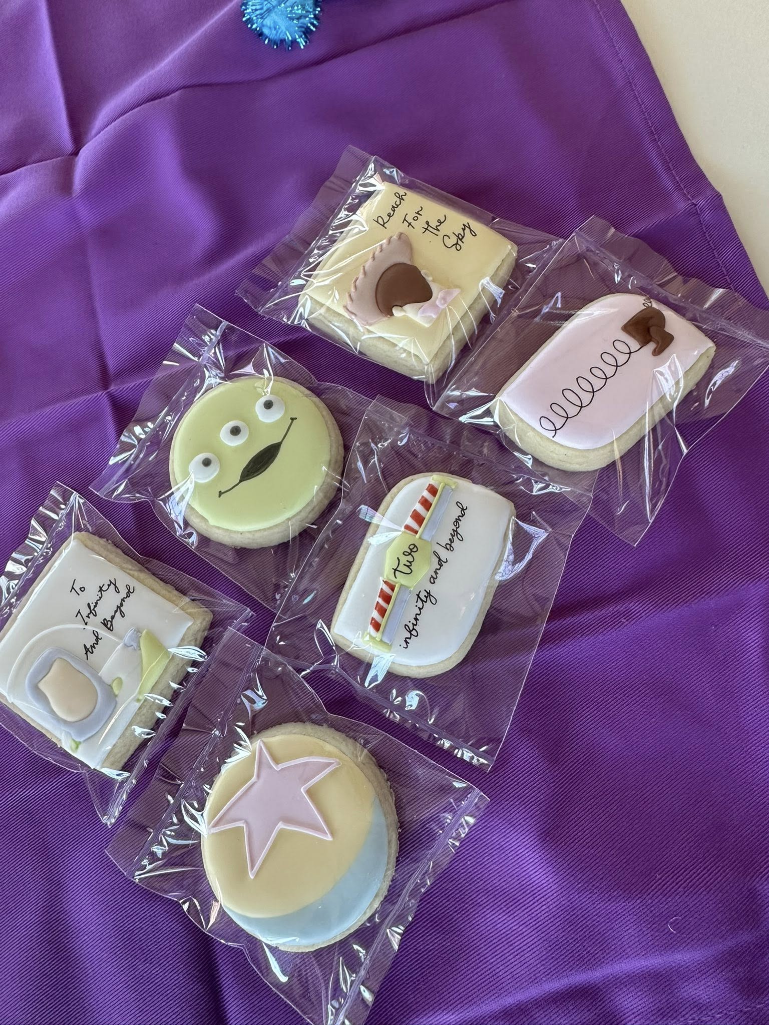 Individually wrapped Toy Story themed sugar cookies decorated with iconic character designs on a purple background.