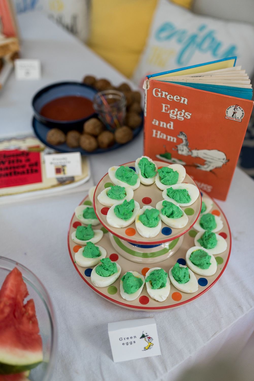 Two-tiered stand filled with green-dyed deviled eggs near a copy of the book Green Eggs and Ham.
