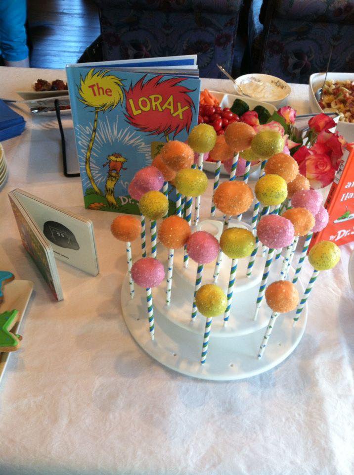 Colorful cake pops arranged on a tiered stand at a Lorax-themed party with a Dr. Seuss The Lorax book nearby.