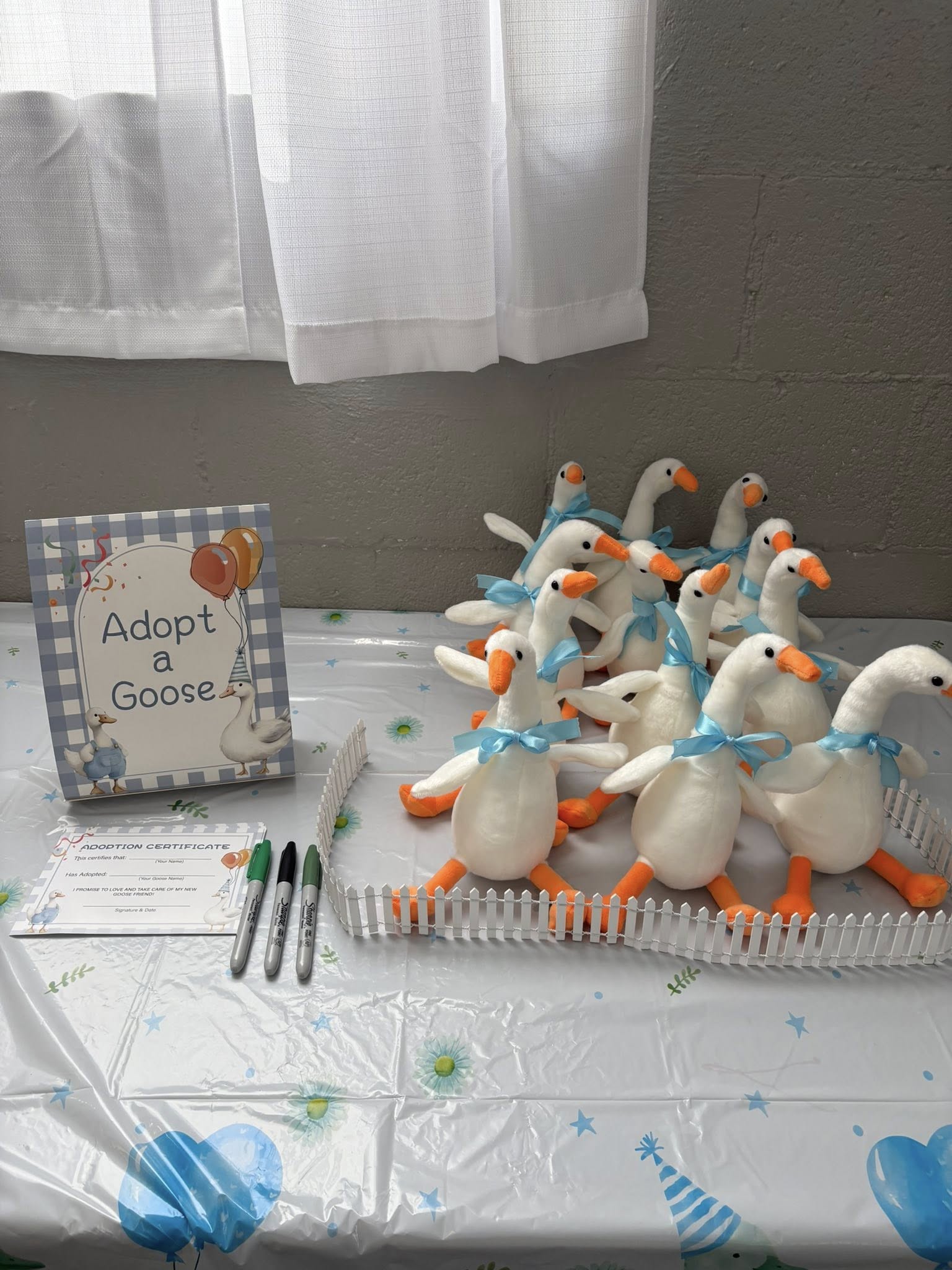 Adopt a Goose party station featuring several plush stuffed geese in a small white fence with adoption certificates.