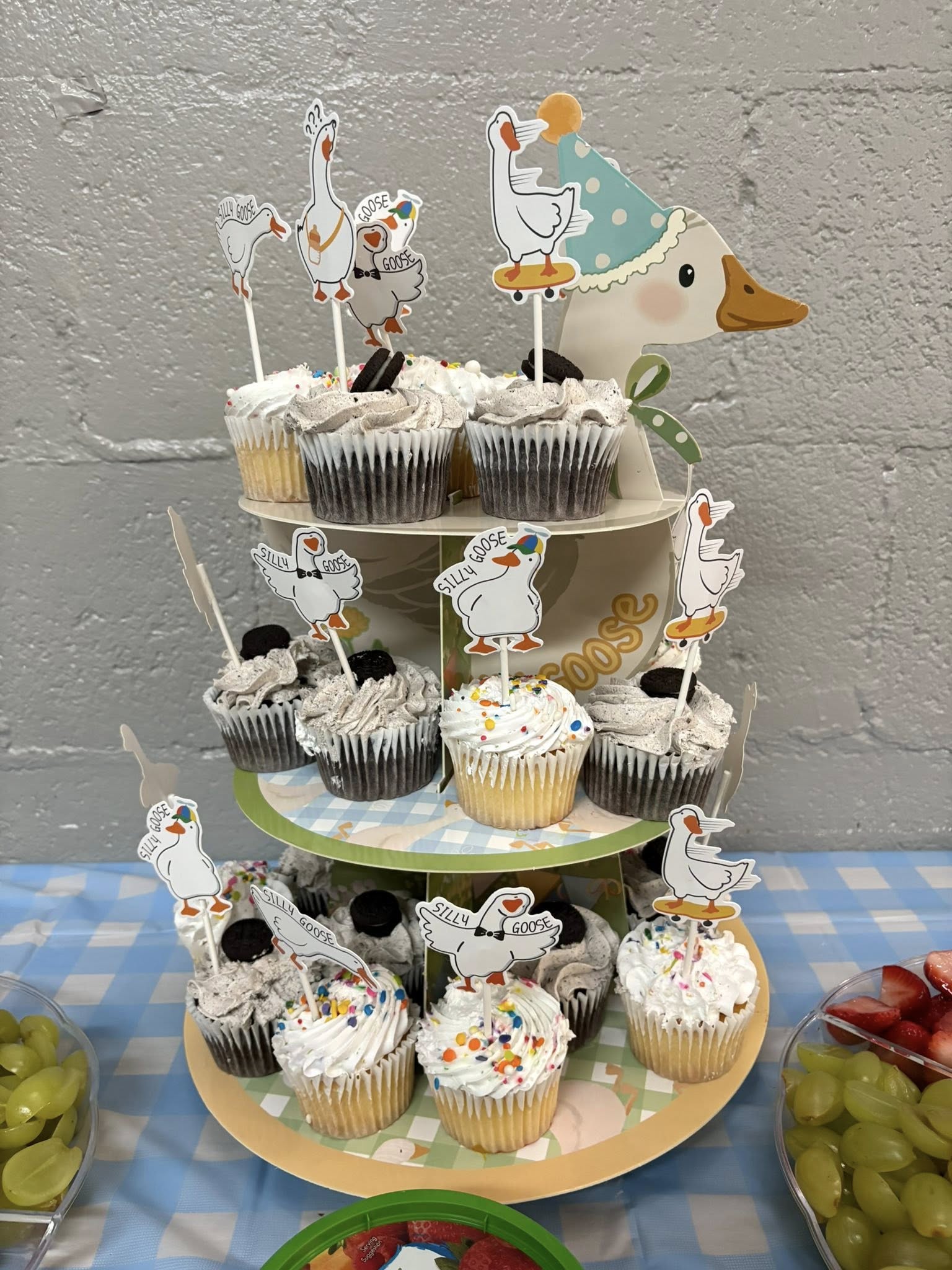 Three-tiered cupcake stand decorated with cute cartoon goose toppers at a party