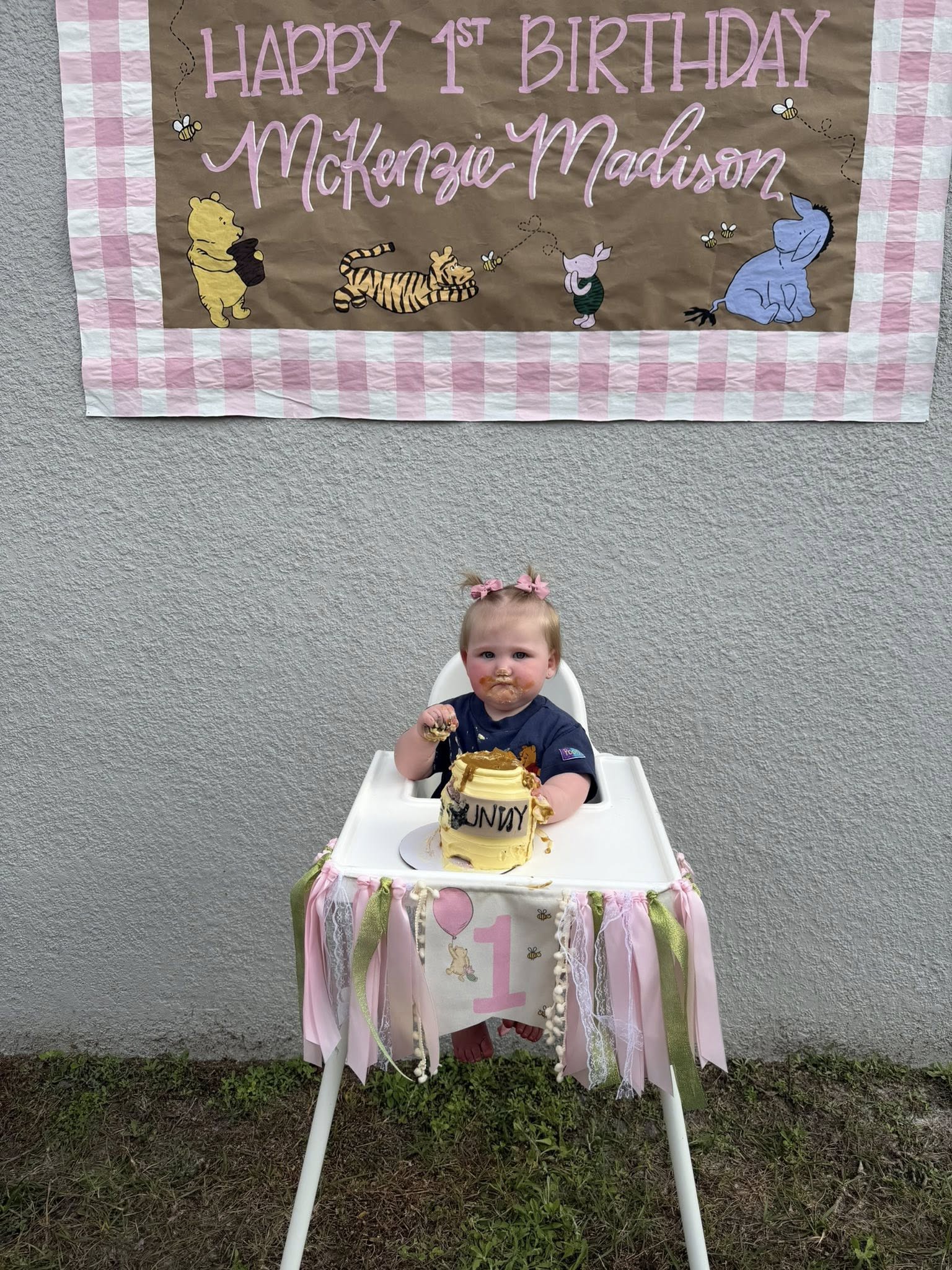 Toddler eating a yellow honey pot cake in a high chair in front of a Winnie the Pooh birthday banner