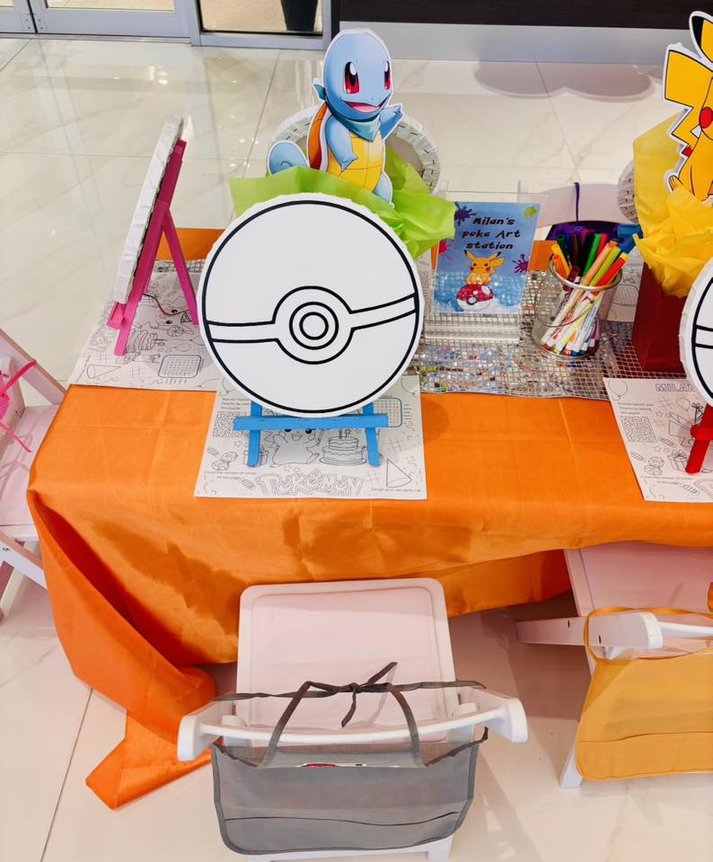 Pokemon-themed art station setup with Poke Ball canvases, Squirtle cutout, and coloring sheets on an orange table.