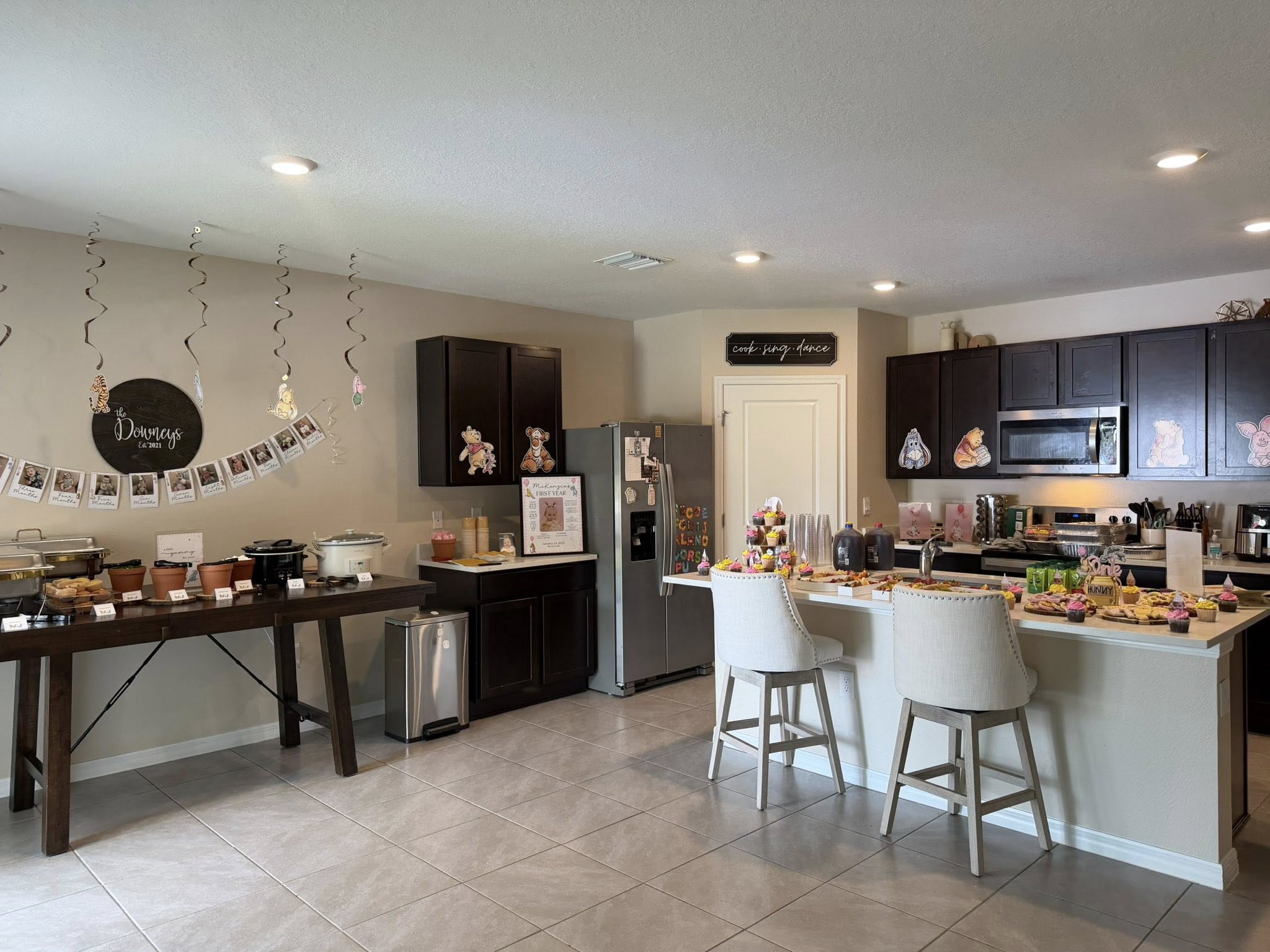 Kitchen decorated for a Winnie the Pooh themed first birthday party with food tables and photo banners.