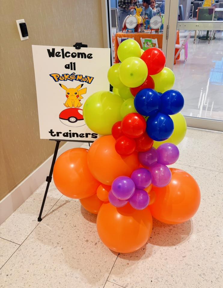 Welcome all Pokemon trainers sign decorated with a colorful balloon arch