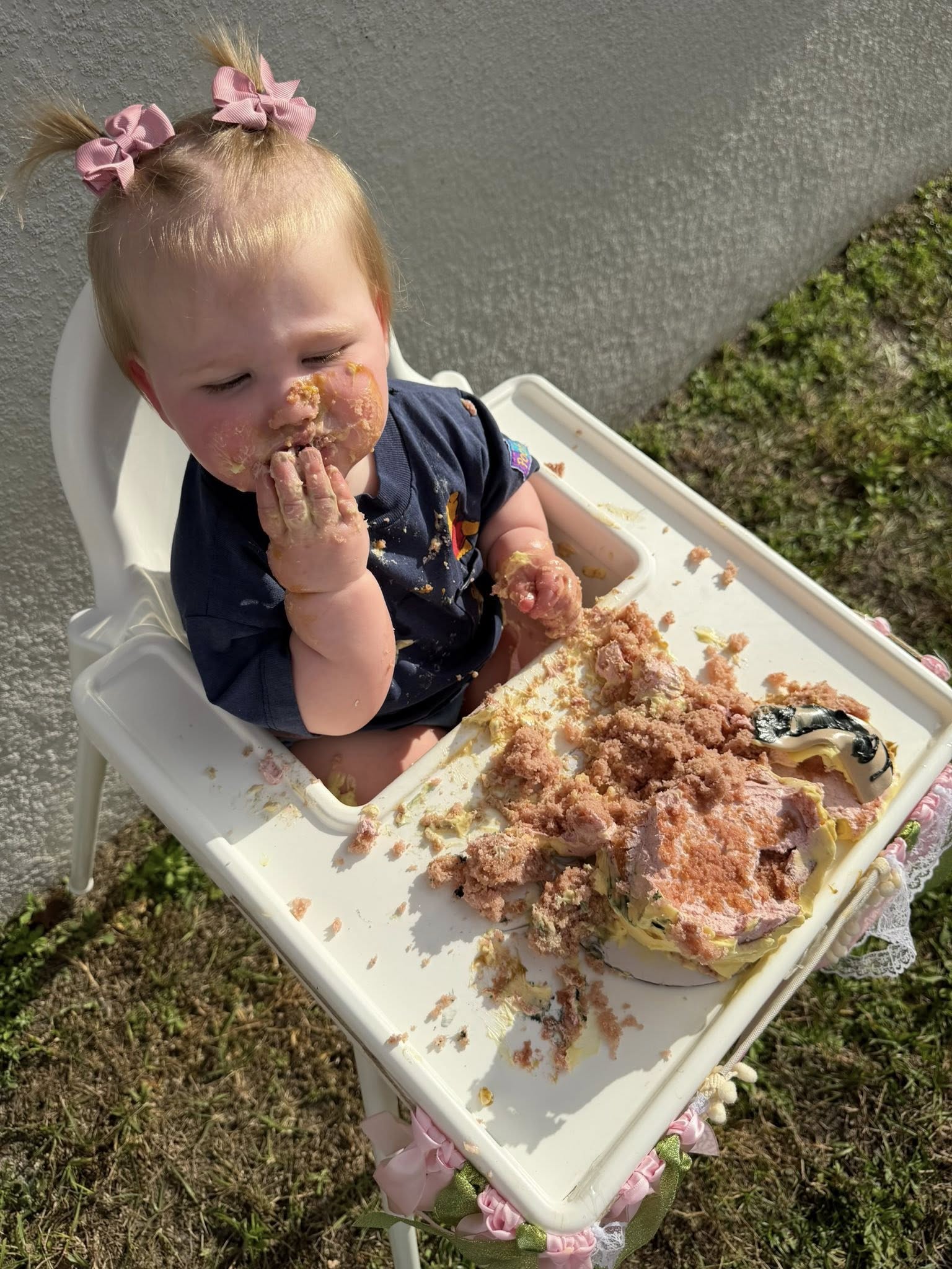 Toddler eating a cake smash birthday cake in a high chair