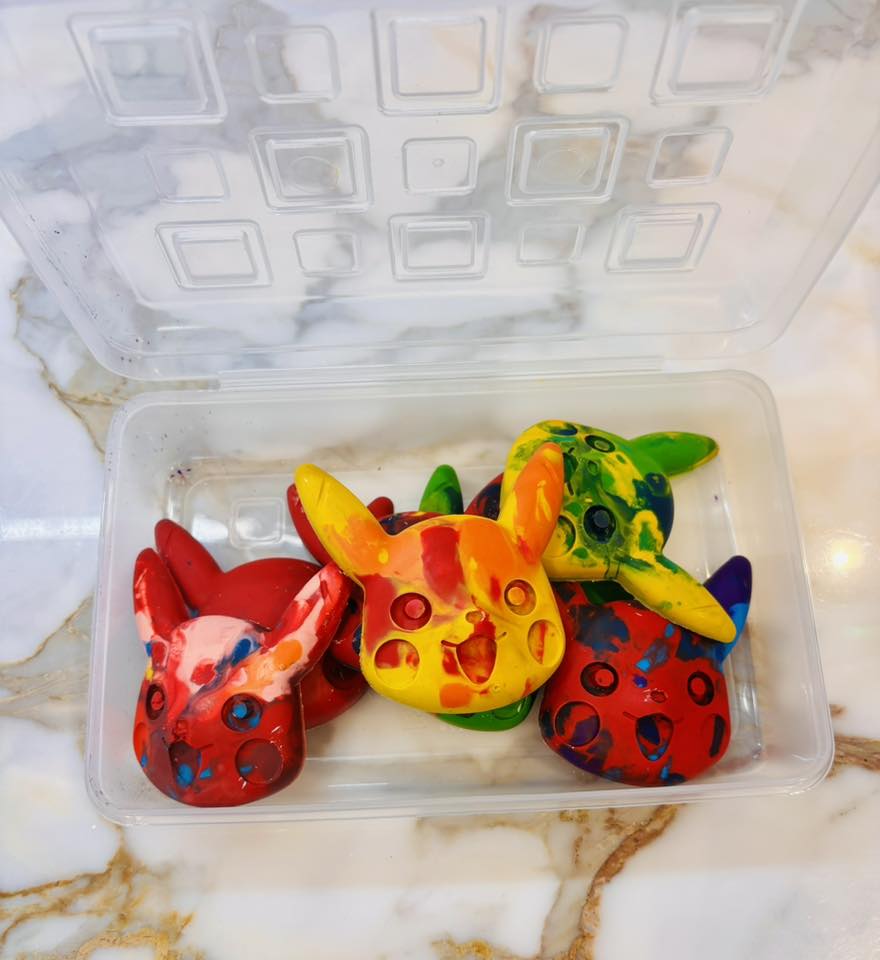 Set of colorful, marbled, Pikachu-shaped handmade crayons in a clear plastic storage container.