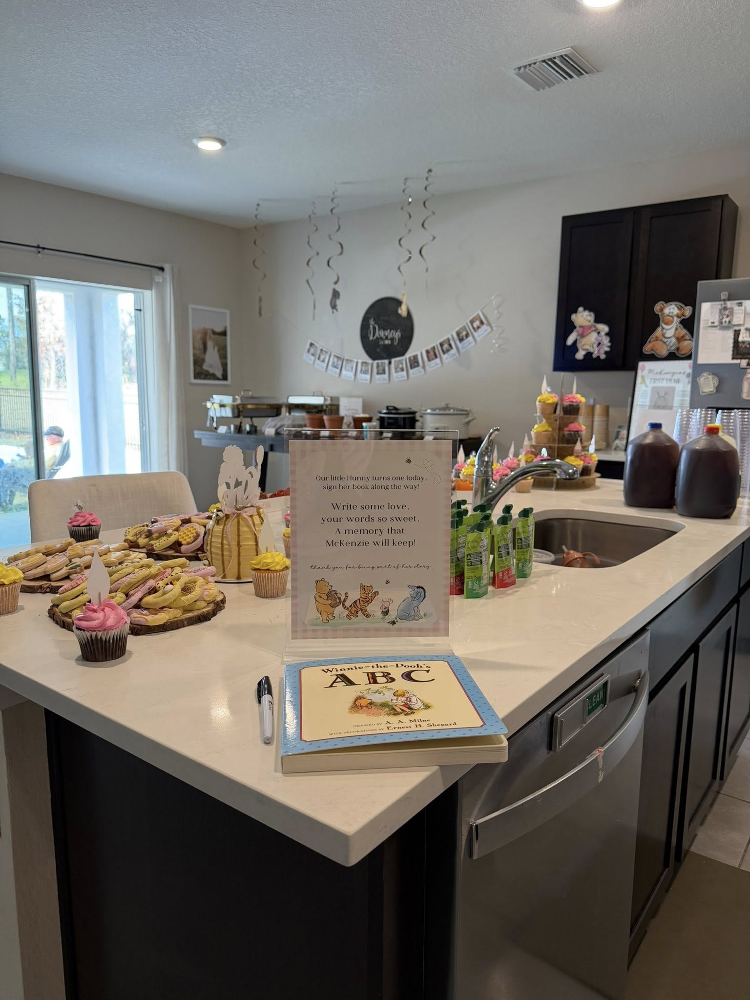 Winnie the Pooh themed first birthday party guest book station with a sign and colorful cupcakes.