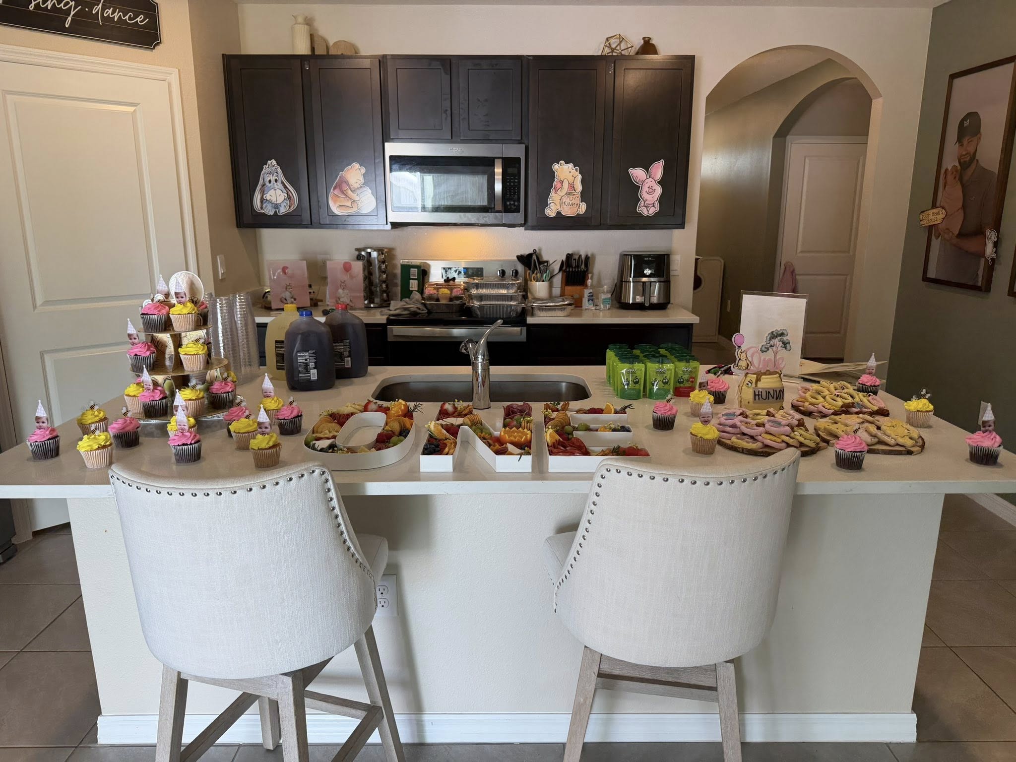 Kitchen counter decorated for a Winnie the Pooh themed birthday party with character-topped cupcakes and snack trays