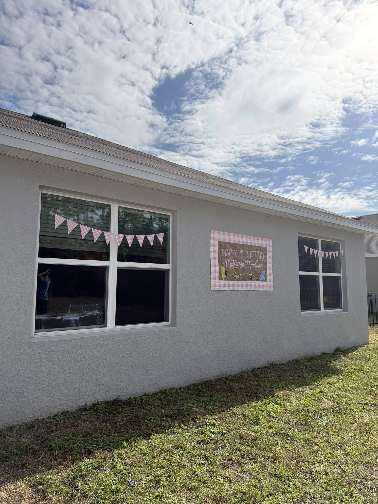 Exterior wall of a house decorated with pink gingham bunting and a Winnie the Pooh first birthday sign.