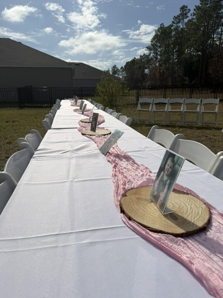 Long outdoor banquet table set for a celebration with pink runners, wood slab centerpieces, and photo frames.