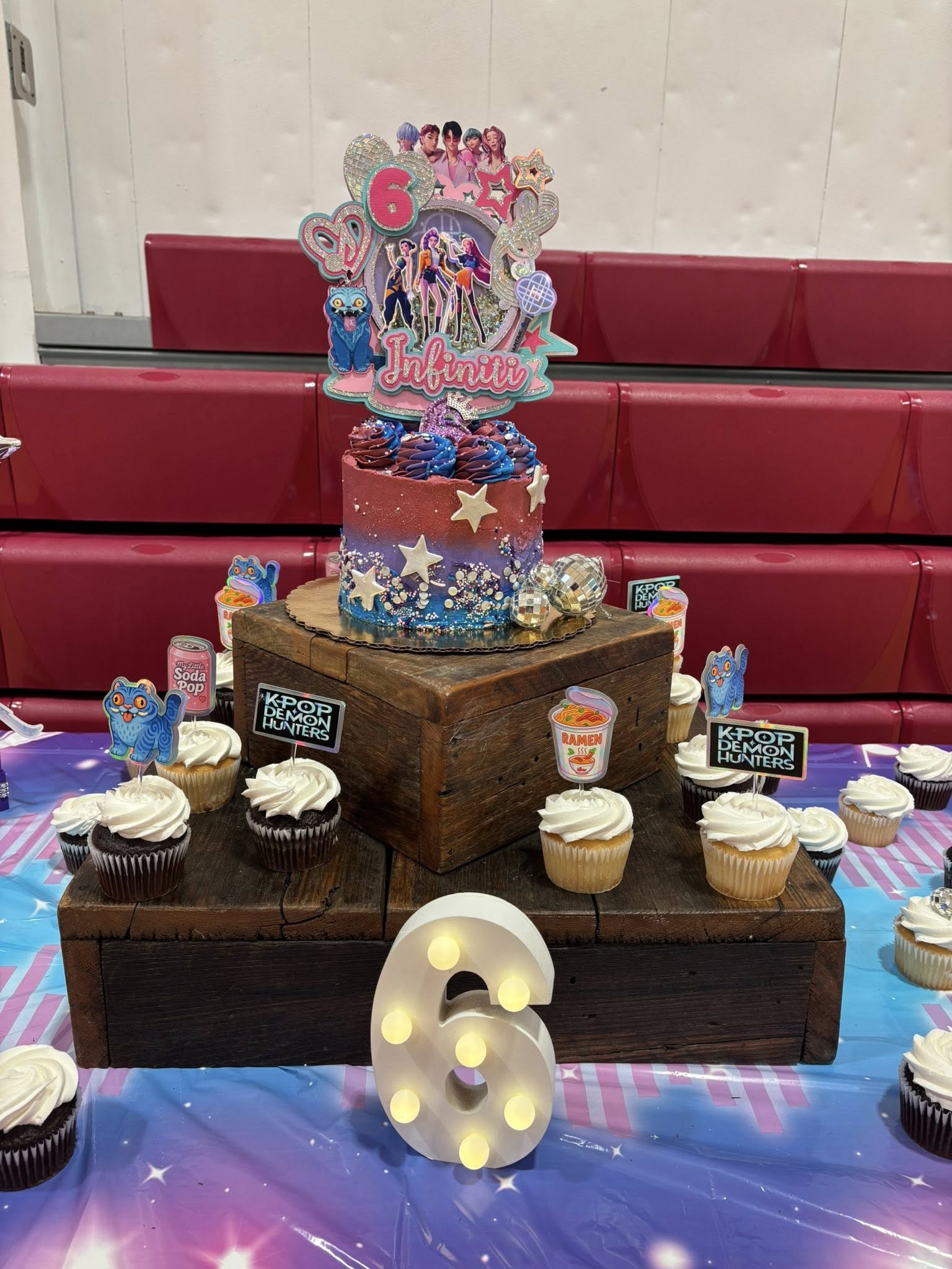 Birthday cake and cupcakes with K-Pop Demon Hunters themed toppers on a rustic tiered display