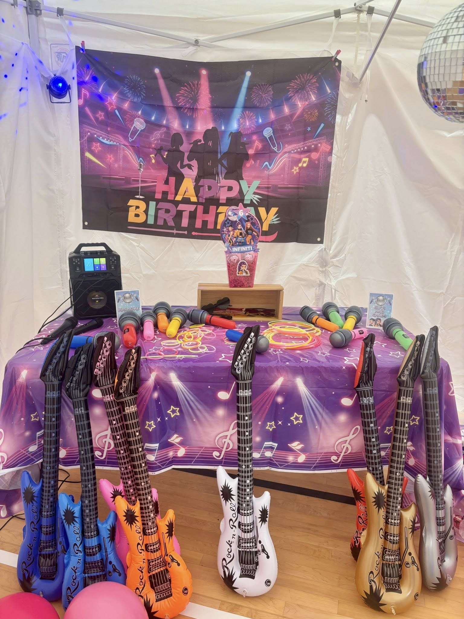 Table set up for a karaoke birthday party featuring inflatable guitars, microphones, and music-themed decorations.