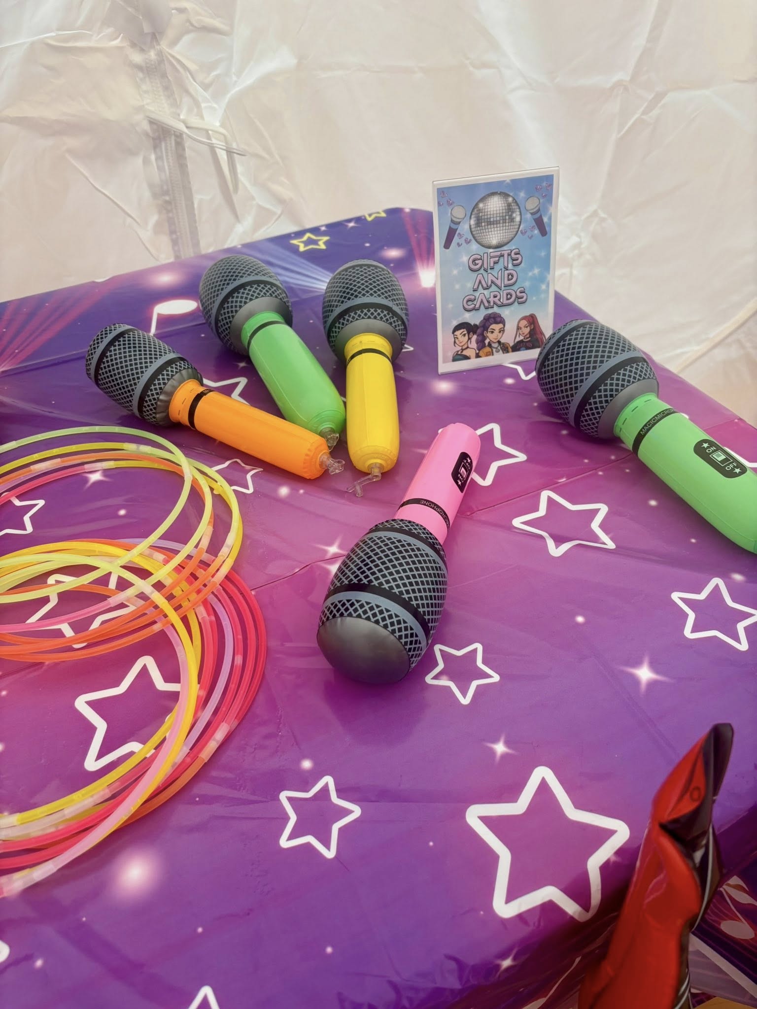 Colorful inflatable toy microphones and glow sticks on a purple star-patterned table with a Gifts and Cards sign.