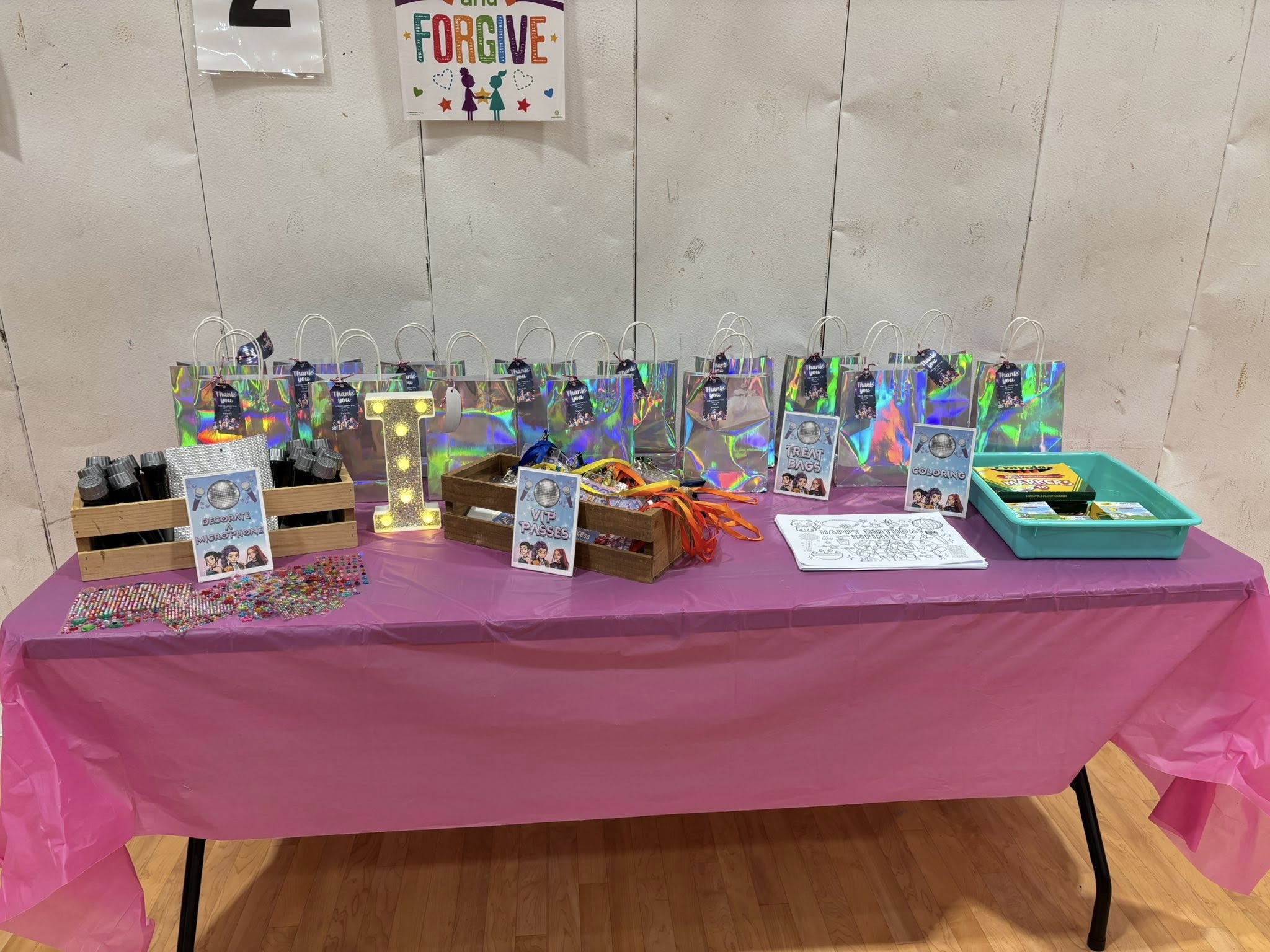 Table arranged with colorful treat bags, microphone decoration supplies, and activity stations for a party.