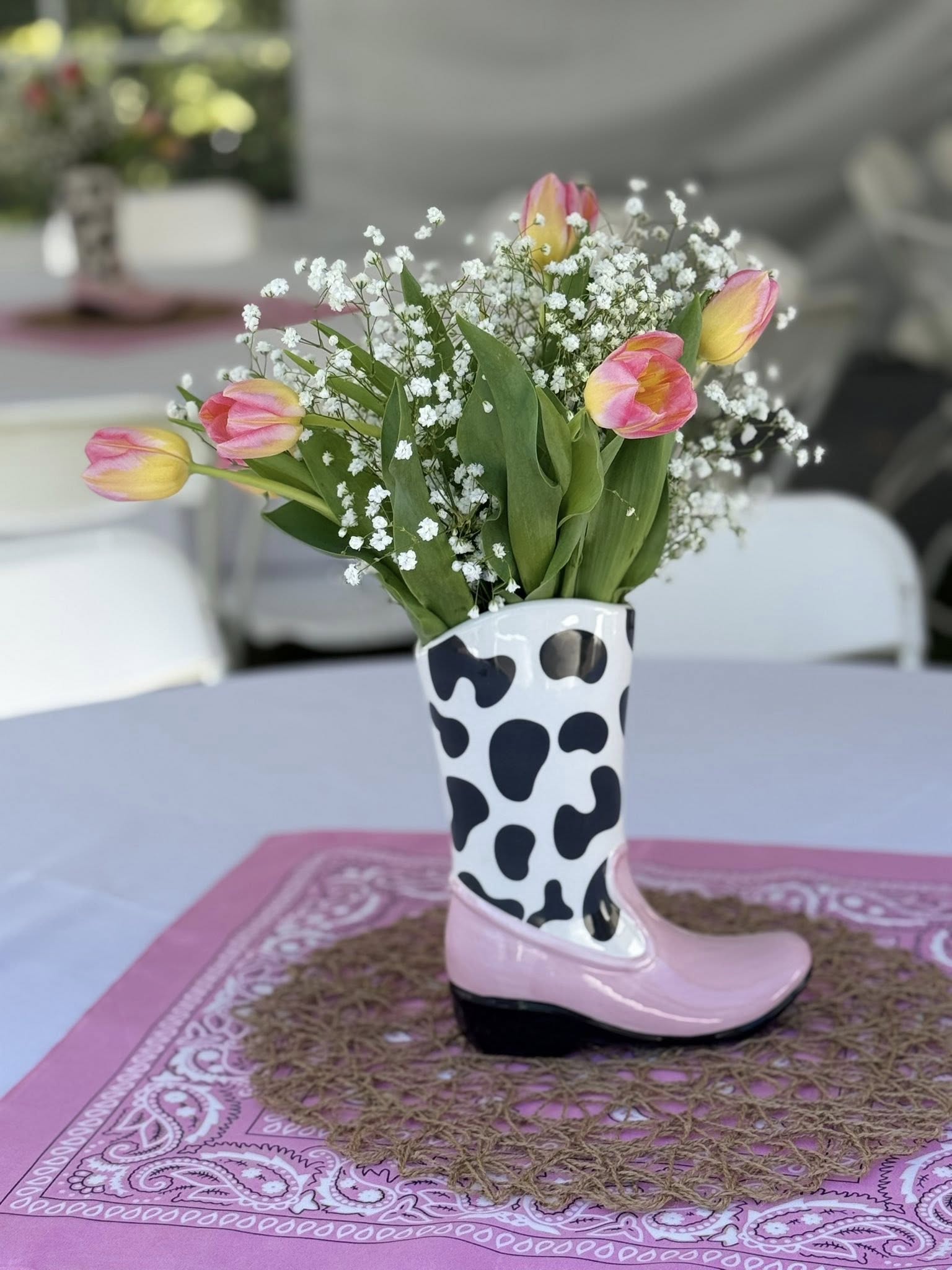 Ceramic cowboy boot vase with cow print and pink accents filled with pink tulips and baby's breath.