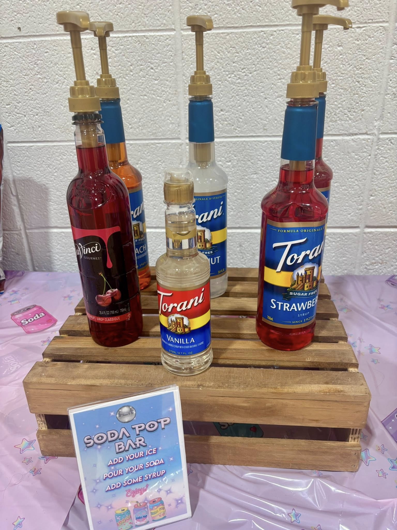 Assorted Torani and DaVinci syrup bottles with pumps on a wooden crate for a DIY soda pop bar.