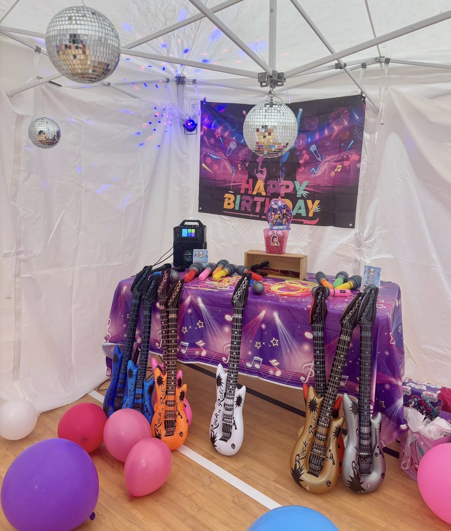 Rock and roll themed birthday party setup with inflatable toy guitars, disco balls, and karaoke machine.