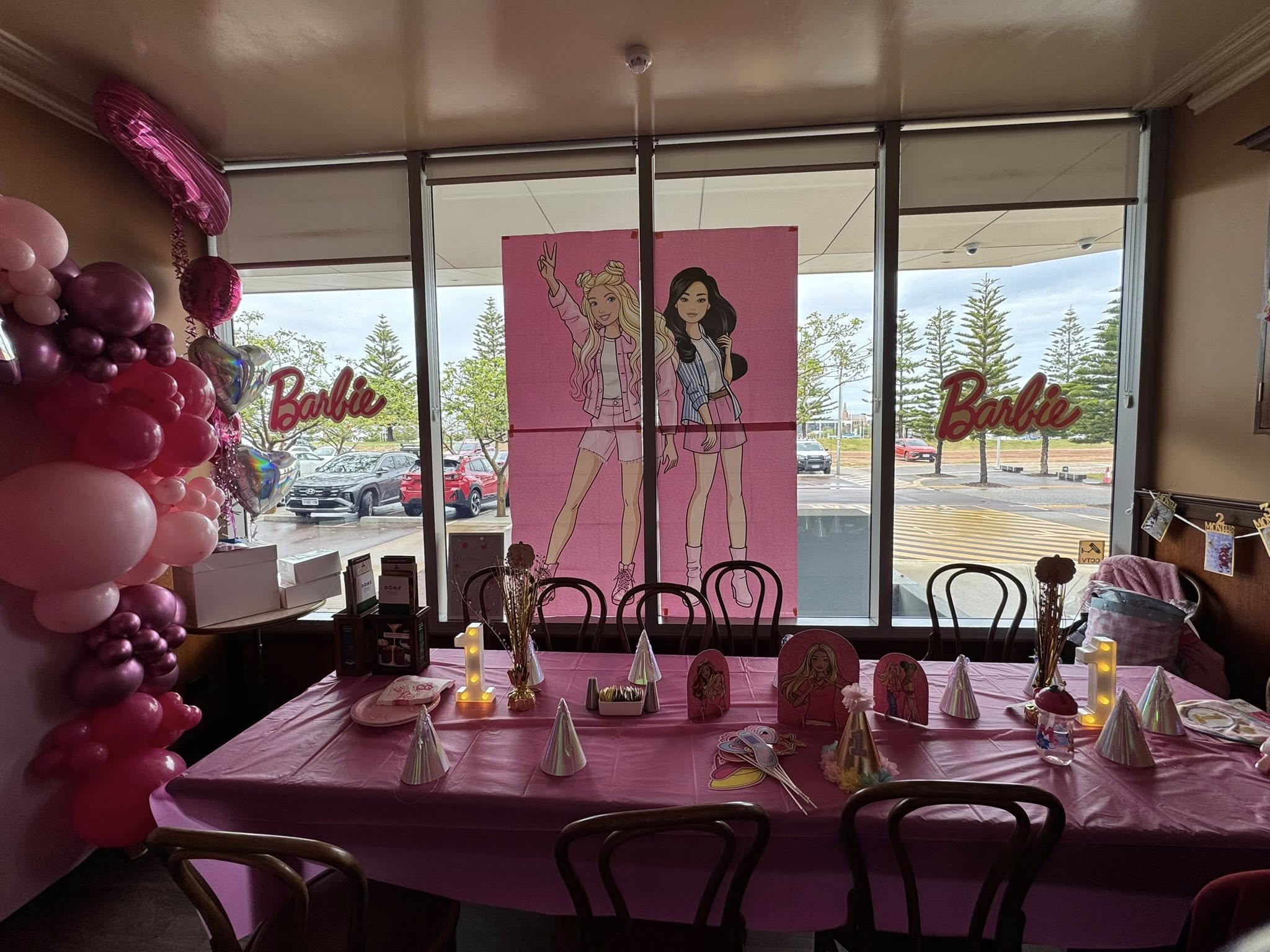 Barbie themed birthday party setup with pink tablecloth decorations balloons and wall posters