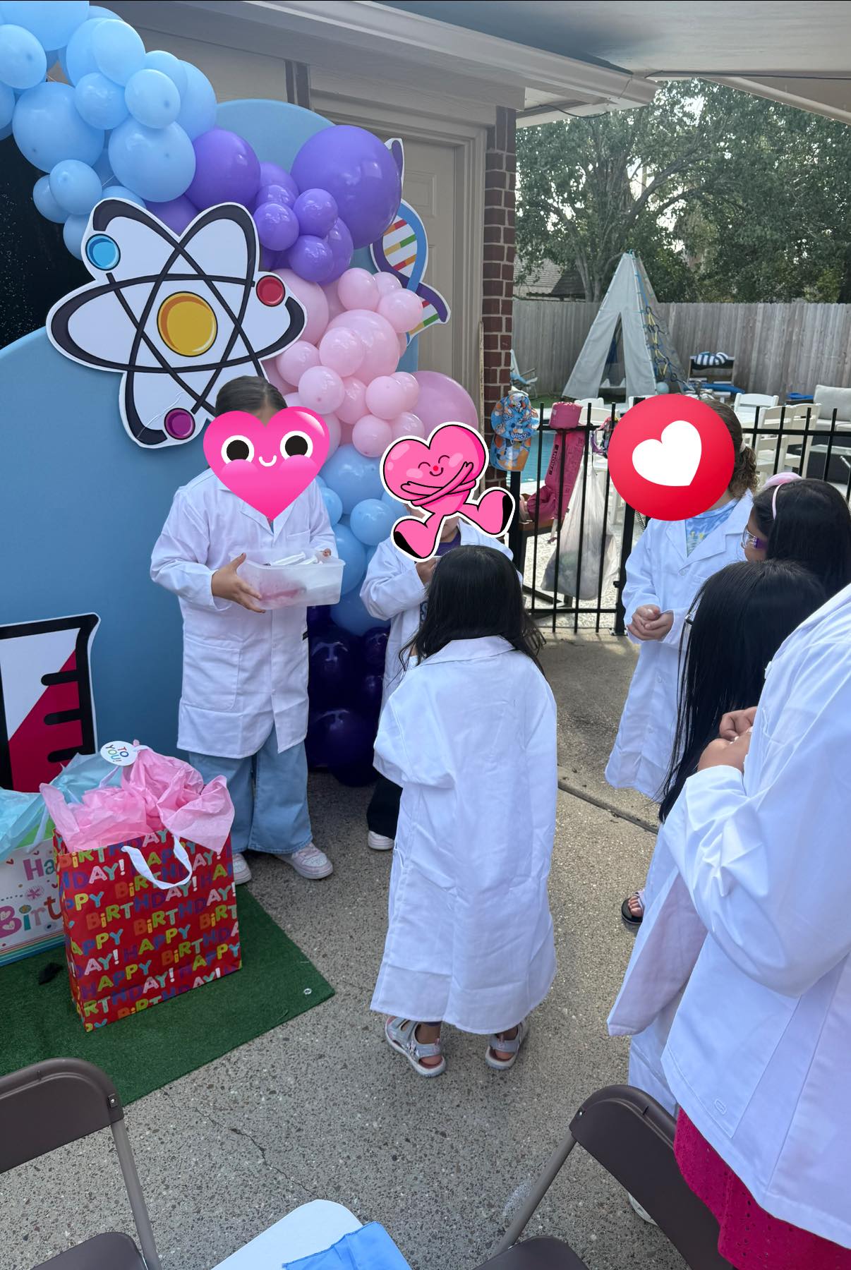 Children wearing white lab coats at a science-themed birthday party with balloon decorations.