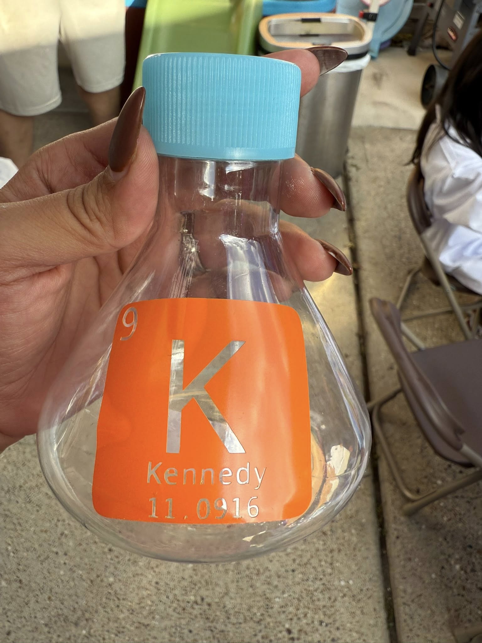 Personalized transparent plastic flask with an orange label featuring the letter K, number 9, and name Kennedy.