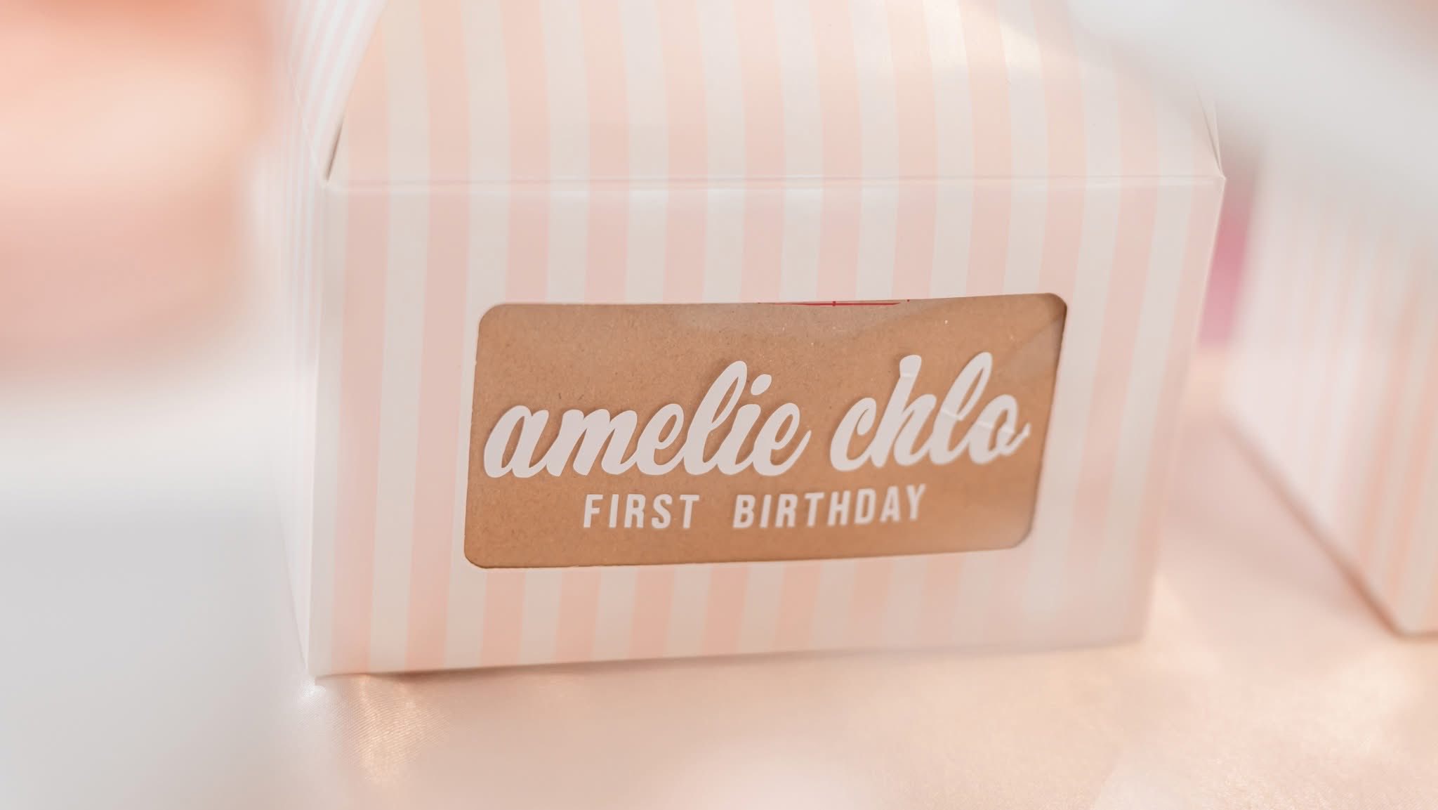Pink and white striped favor box labeled Amelie Chlo First Birthday