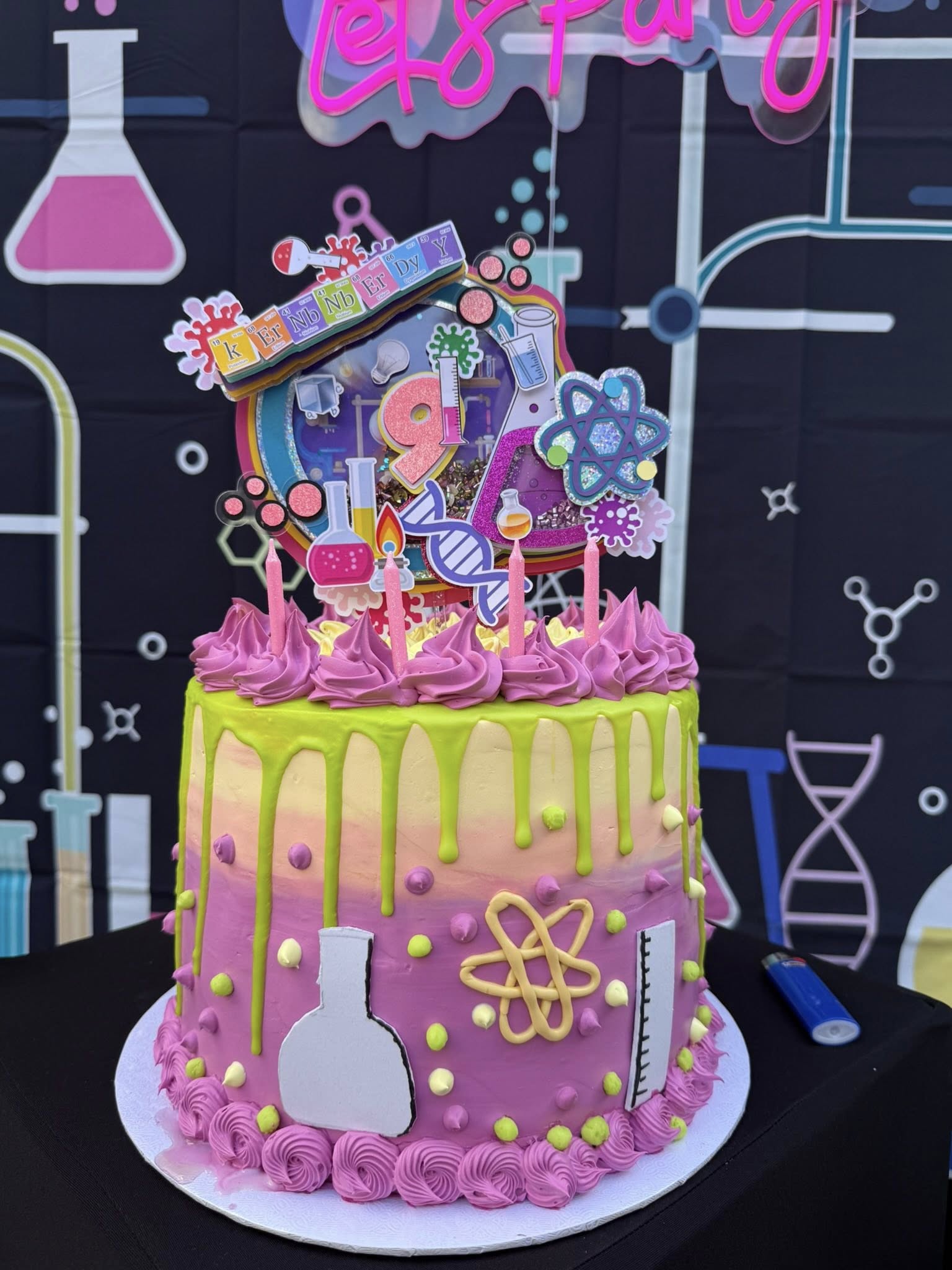 Colorful science-themed birthday cake featuring lab equipment decorations, a periodic table topper, and the number 9.