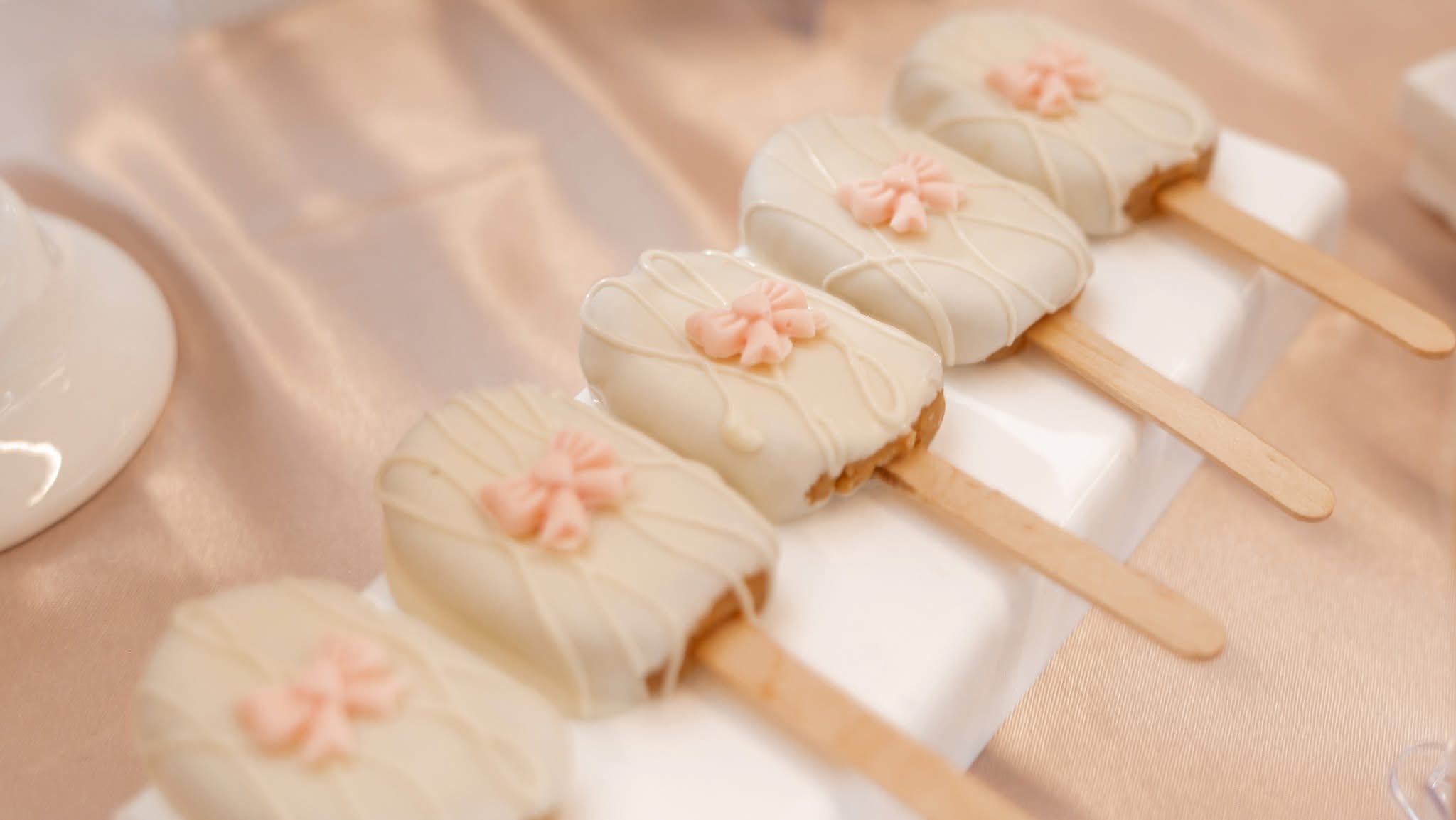 White chocolate covered cake pops with pink bow decorations on sticks