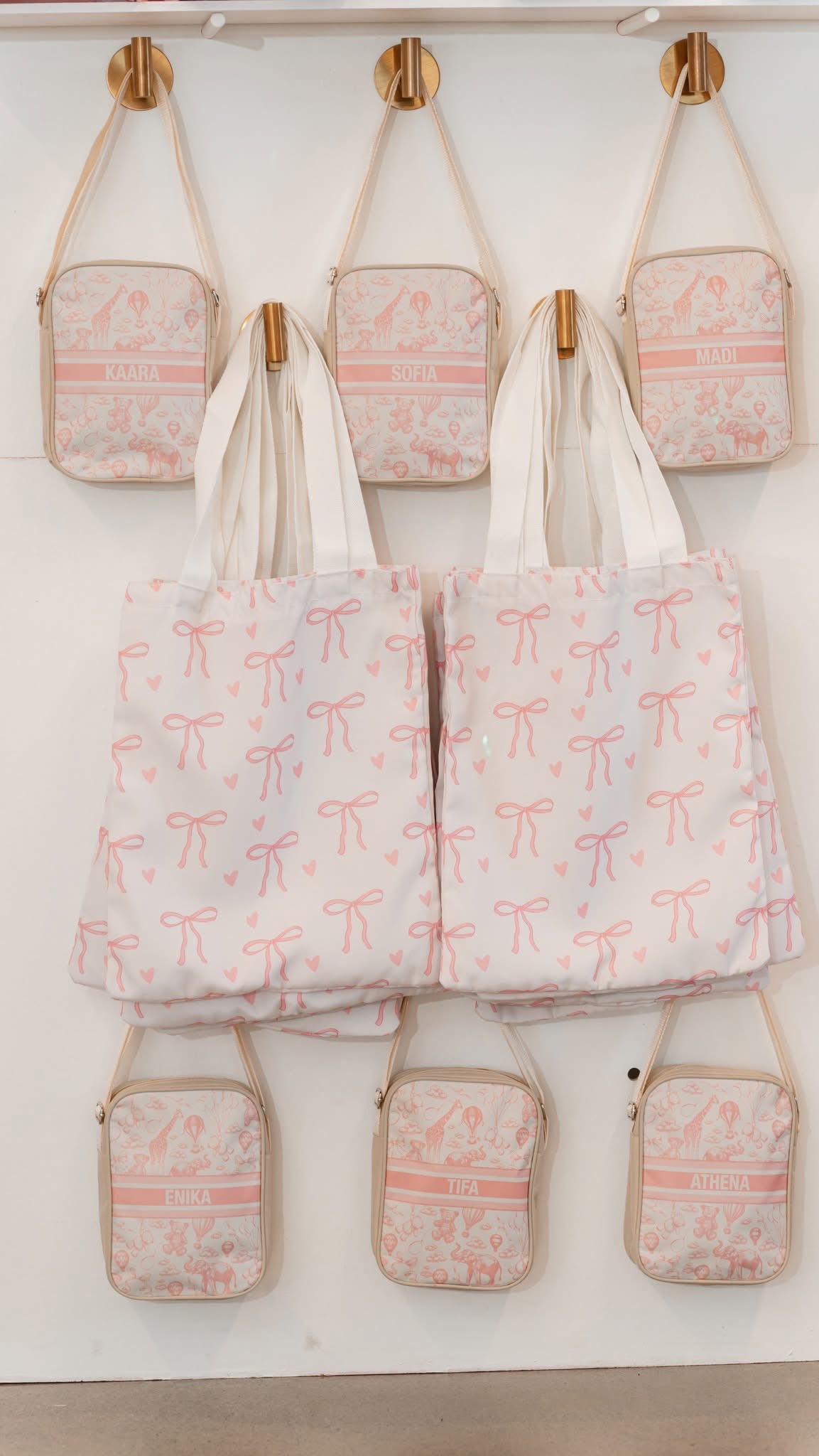 Personalized small crossbody bags and larger tote bags with bows on a display wall.
