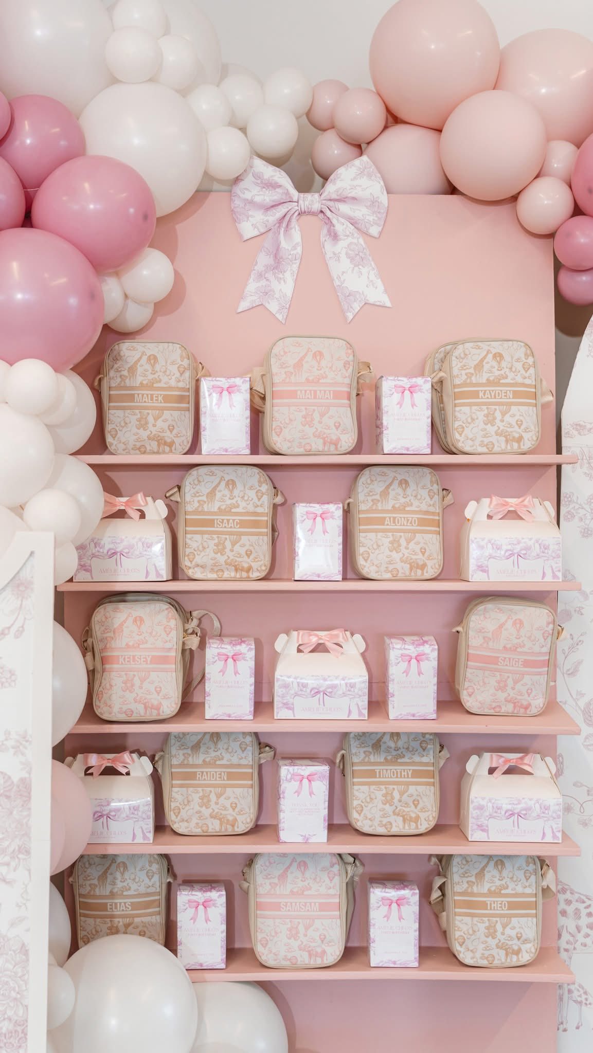 Shelves displaying personalized baby toiletry bags and gift boxes with a pink safari theme and balloon arch.