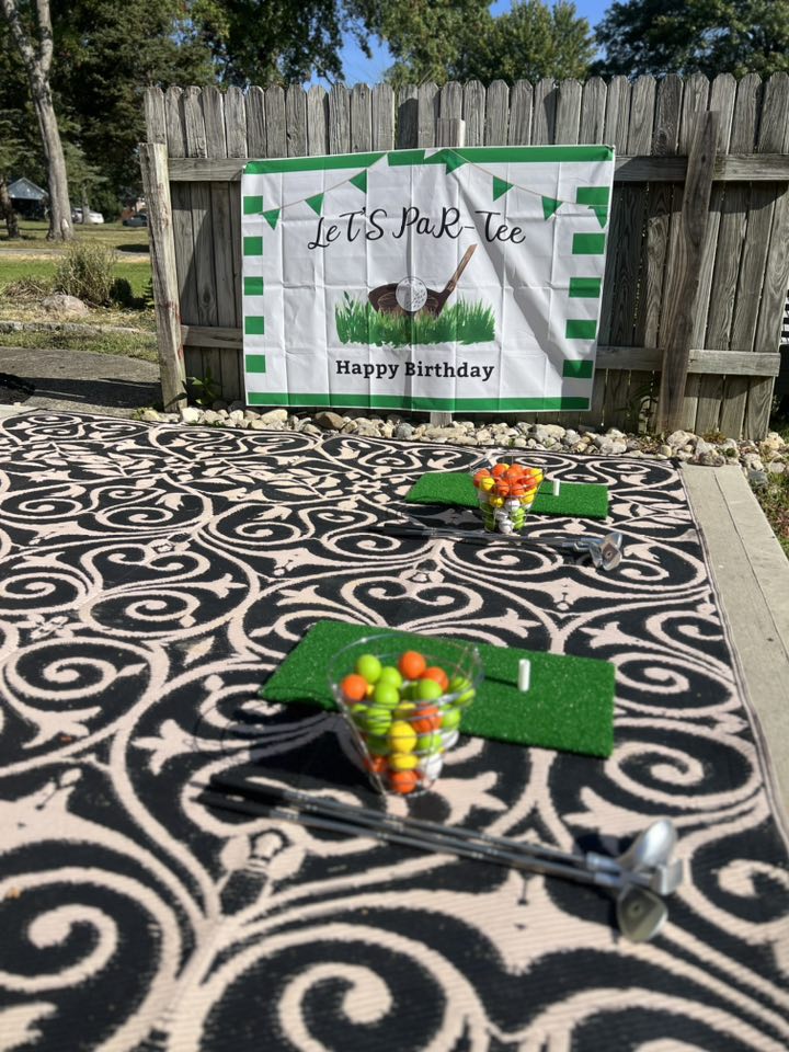 Let's Par-Tee golf birthday backdrop with putting green mats, golf clubs, and colorful golf balls.