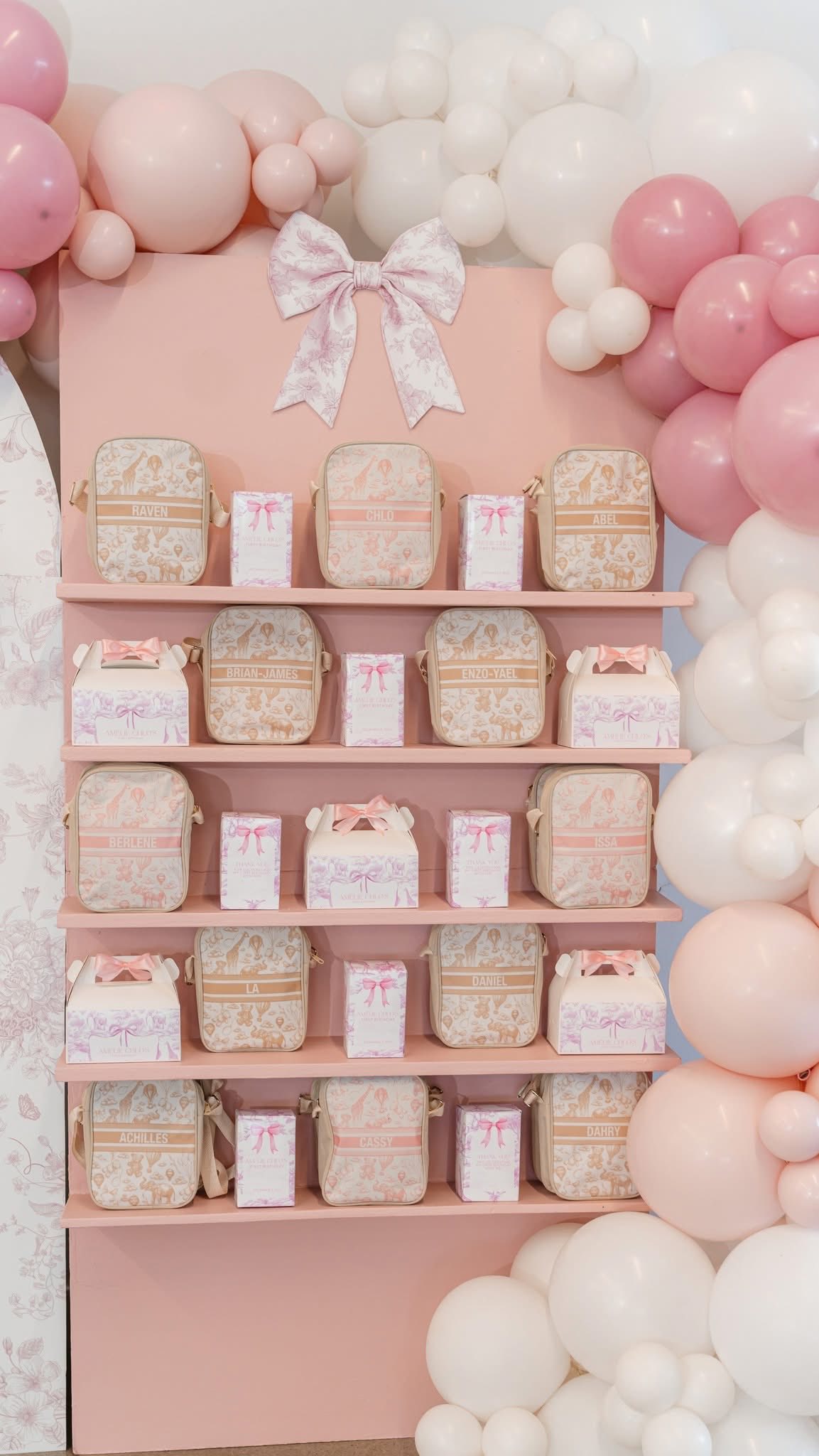 Shelves displaying personalized gift bags and boxes with a pink safari print and bow accents for a birthday party.