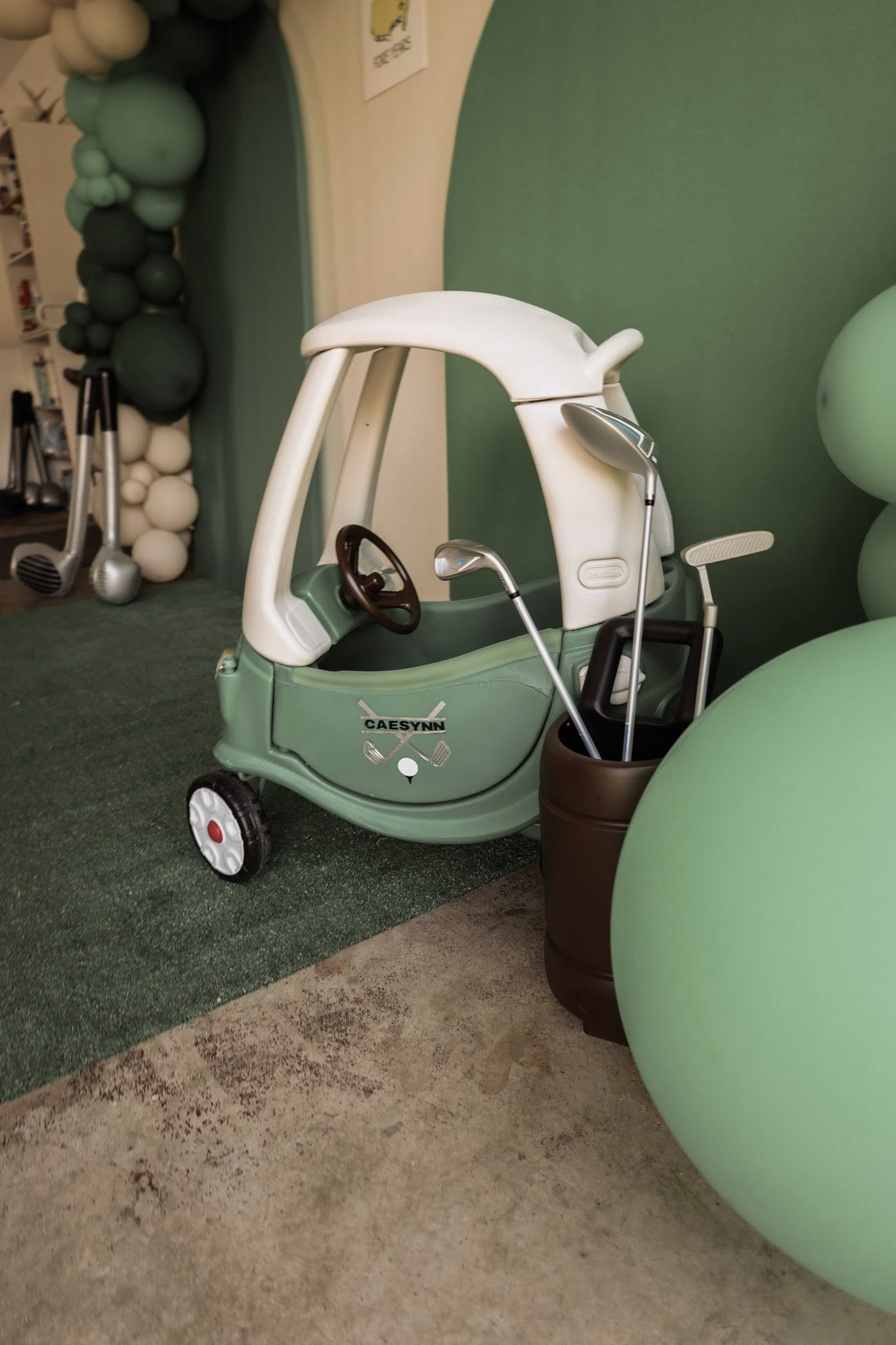 Customized green toy push car decorated for a golf-themed party with a personalized Caesynn sticker and golf clubs.