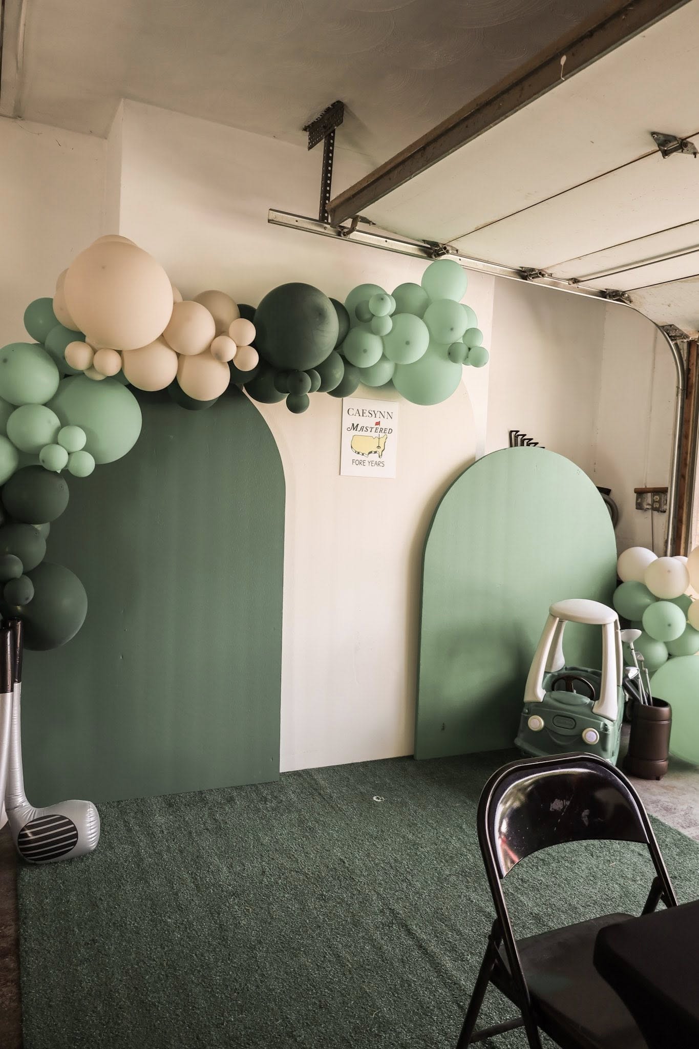 Golf-themed party backdrop with arched green panels, green and cream balloon garland, and decorative party supplies.