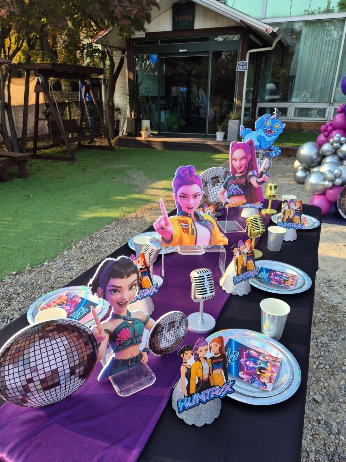 Table decorated for a Huntrx theme party with pop star cutouts, disco balls, and miniature microphones.